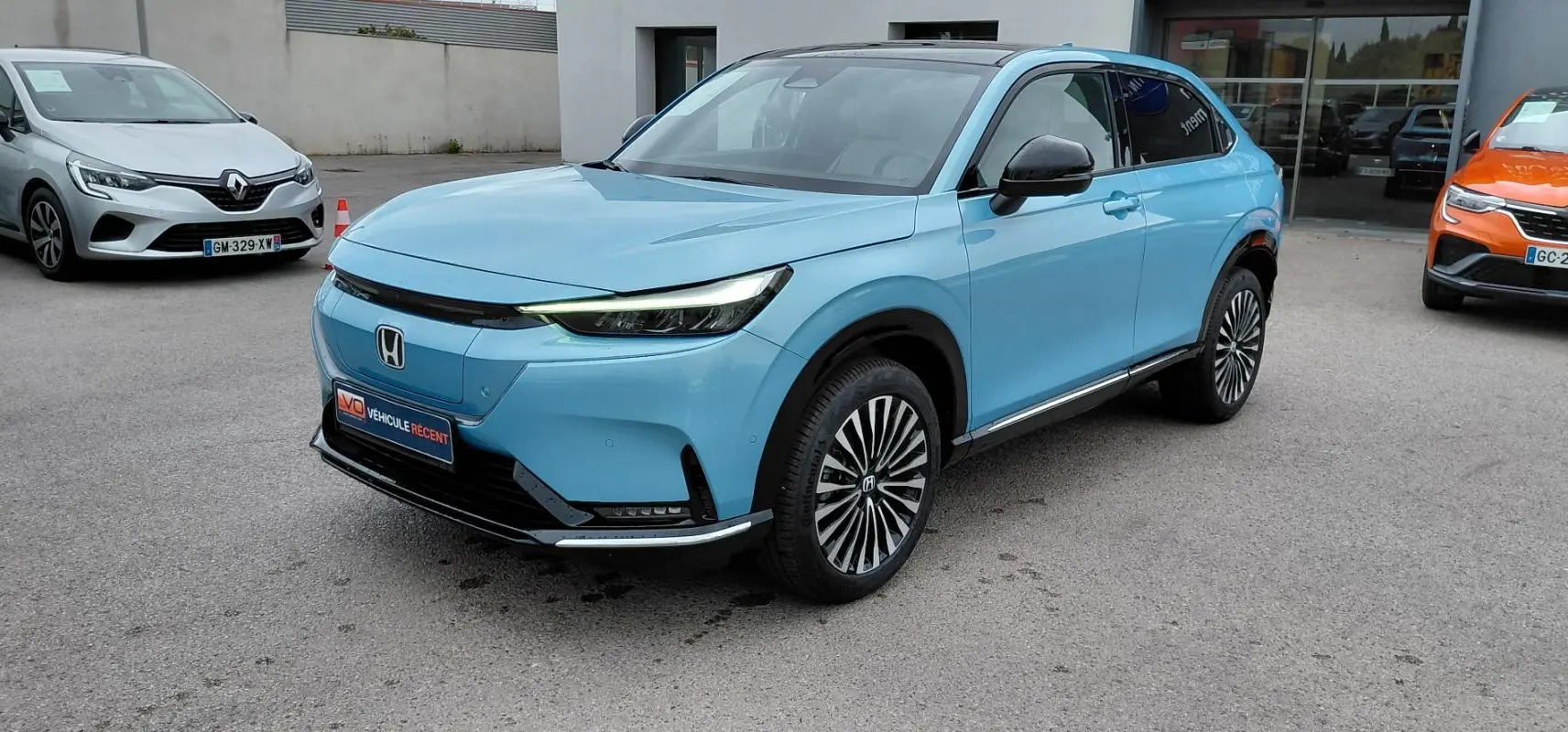 Vue 3/4 avant droite d'un Honda e:Ny1 204 ch Advance bleu électrique avec jantes stylisées et toit noir.