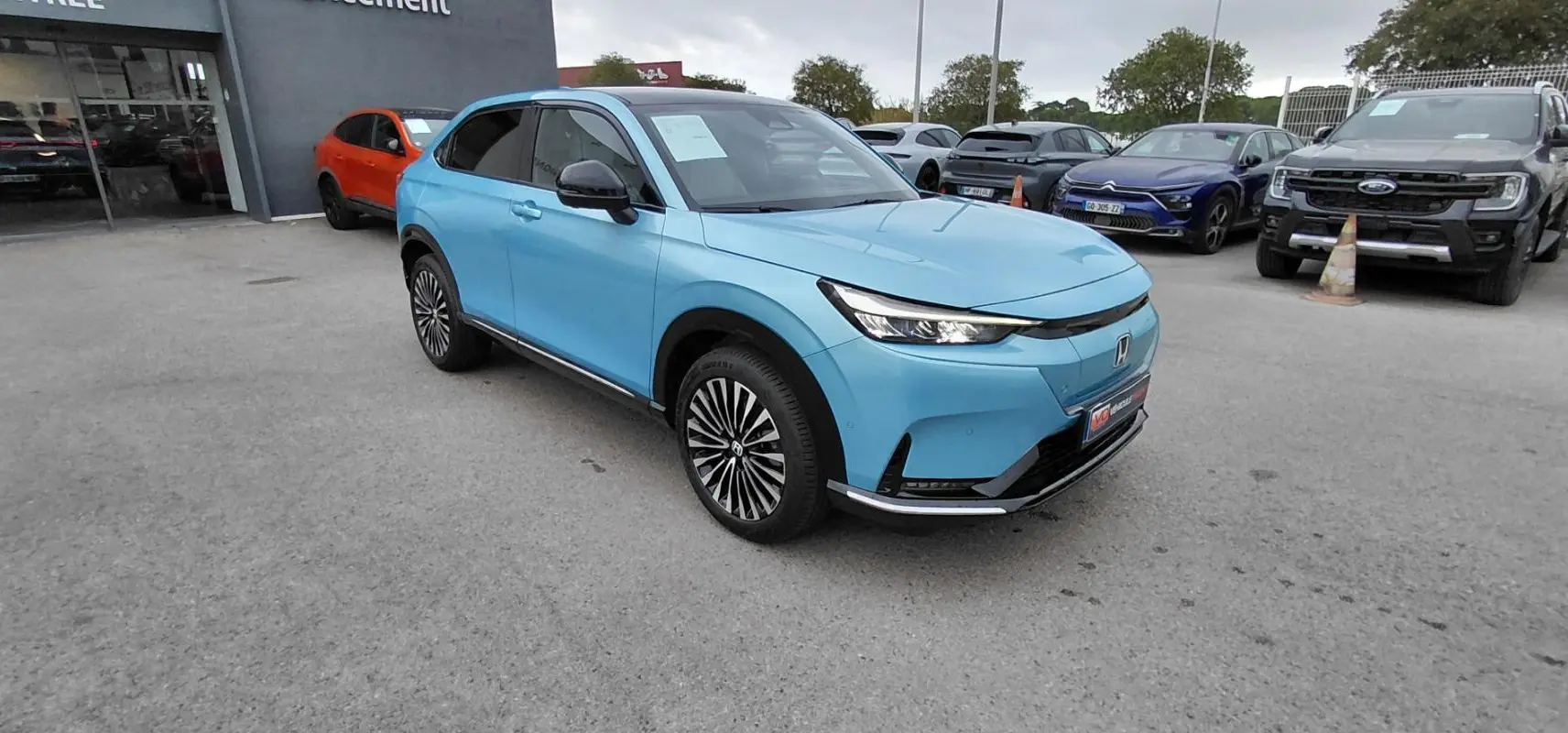 Honda e:Ny1 204 ch Advance bleu en vue 3/4 avant droit, avec jantes distinctives et calandre épurée électrique 2025.
