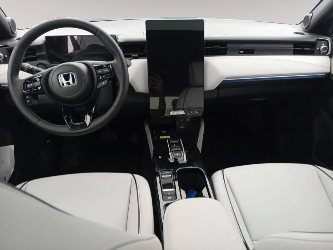 Vue intérieure avant du Honda e:Ny1 204 ch Advance 2025, tableau de bord blanc avec écran tactile vertical et volant noir.