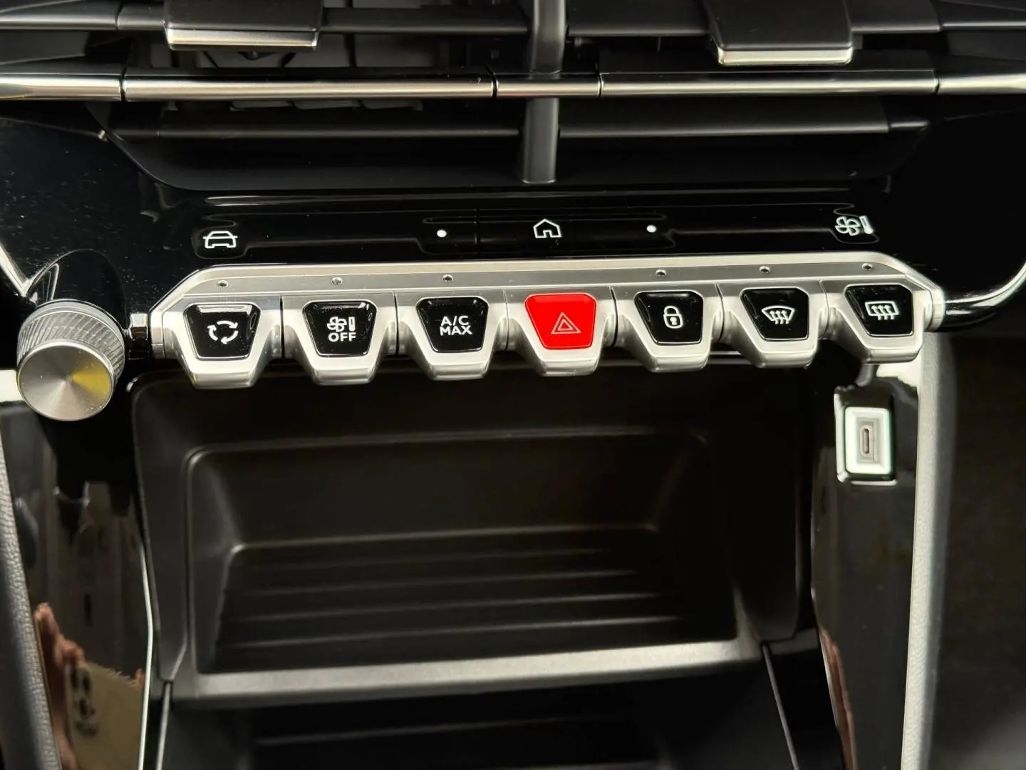 Vue rapprochée des commandes centrales avec boutons argentés et rouge sur tableau de bord noir brillant d'une Peugeot 208.