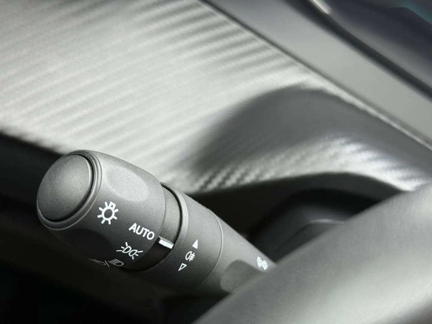 Gros plan sur la commande des phares automatique dans l’habitacle noir de la Peugeot 208 1.2 Hybrid 2025.