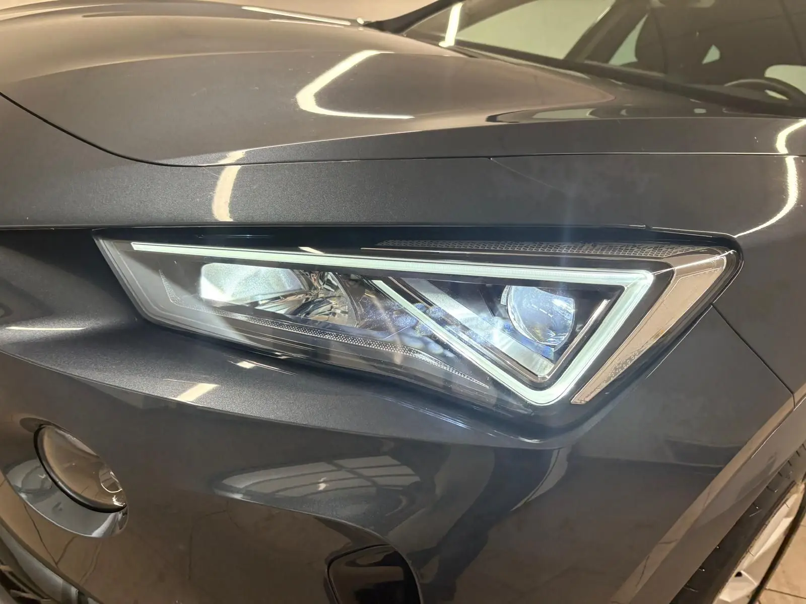 Gros plan sur le phare avant droit du CUPRA Formentor gris magnétique 2024 avec détails LED et carrosserie métallique.