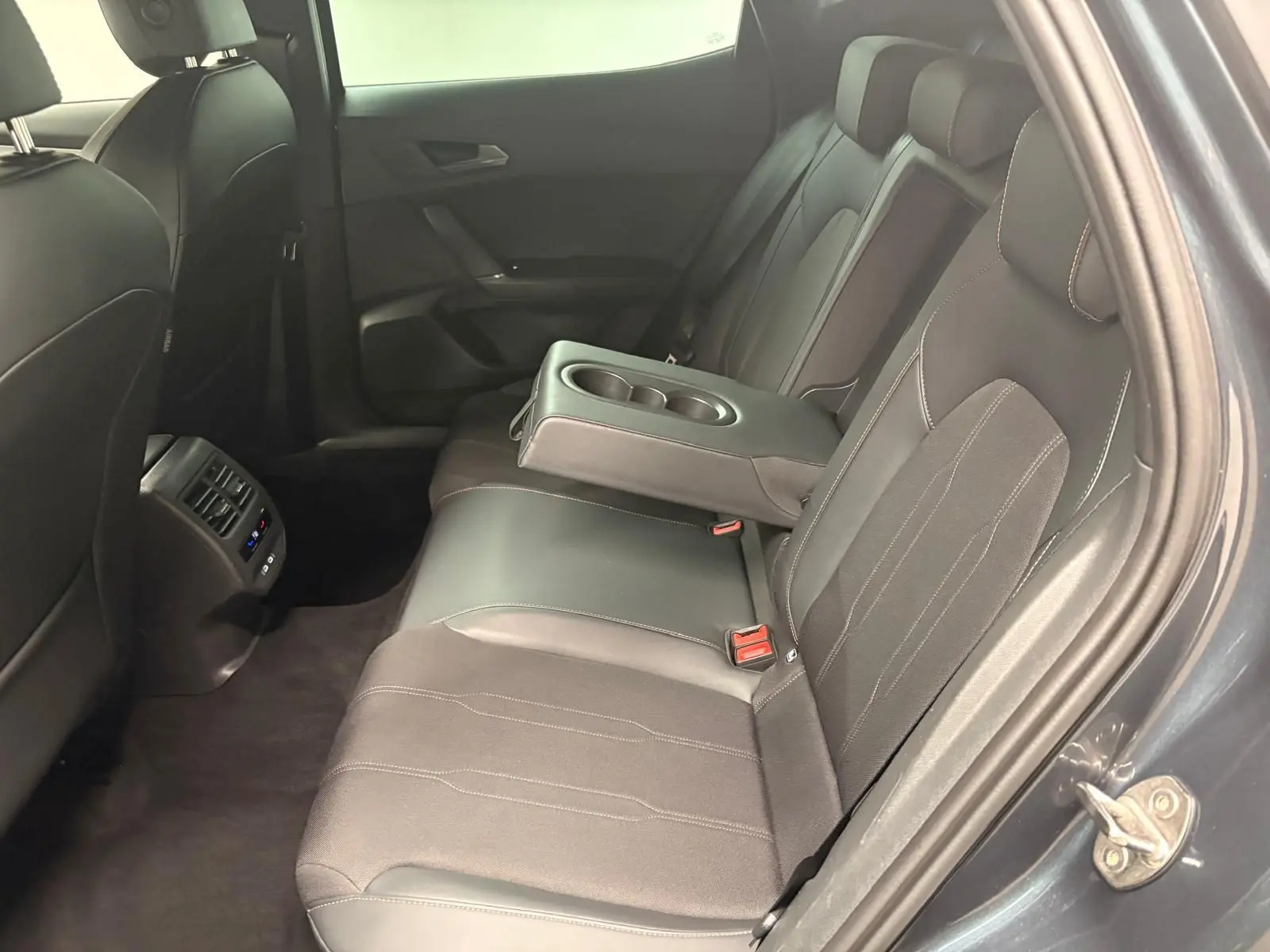 Vue côté droit de l’arrière du CUPRA Formentor gris magnétique, montrant les sièges noirs avec accoudoir central et porte-gobelets.