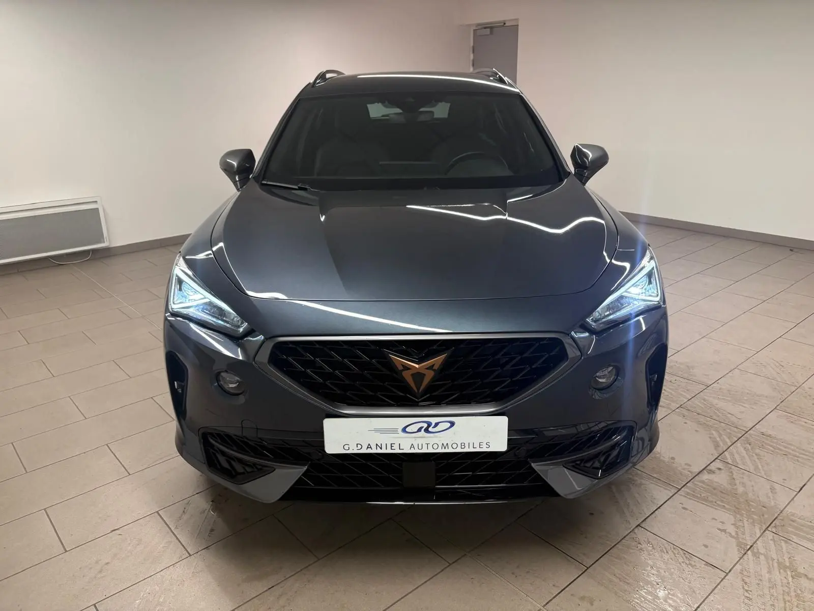 Vue avant d'un CUPRA Formentor gris magnétique 2024 avec calandre noire et feux LED allumés en intérieur.