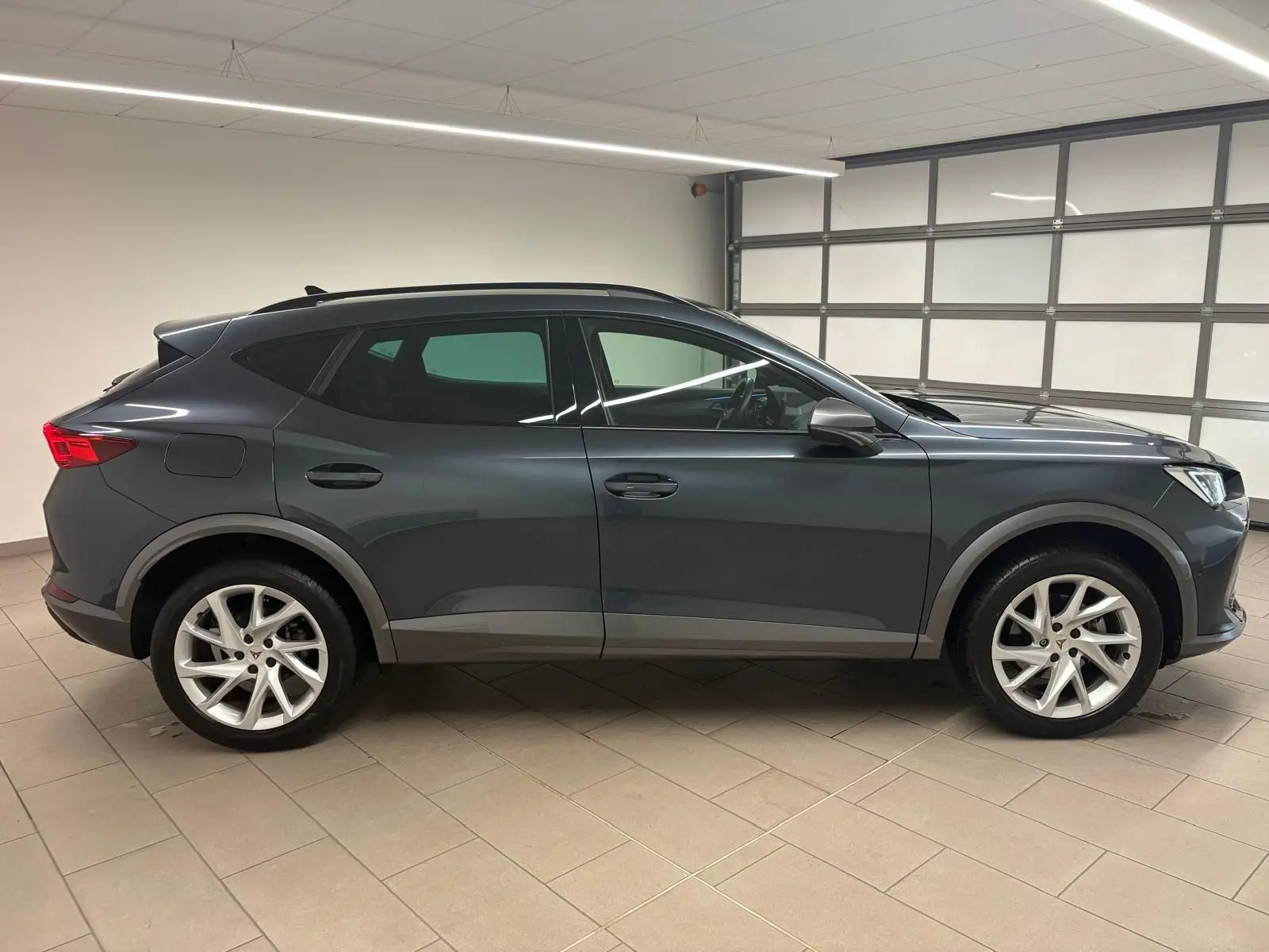 Vue de profil côté gauche d'un CUPRA Formentor 2024 gris magnétique avec jantes argentées en intérieur fermé.