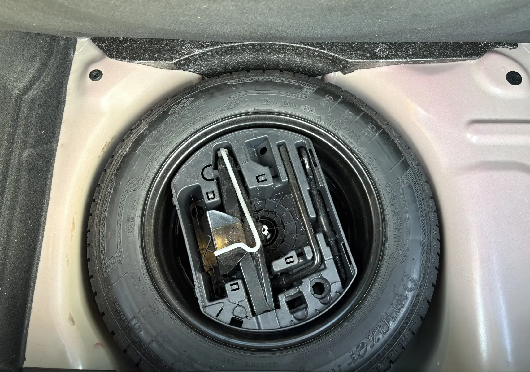 Gros plan sur la roue de secours et les outils de bord dans le coffre d'une Citroën C3 rouge 2018.