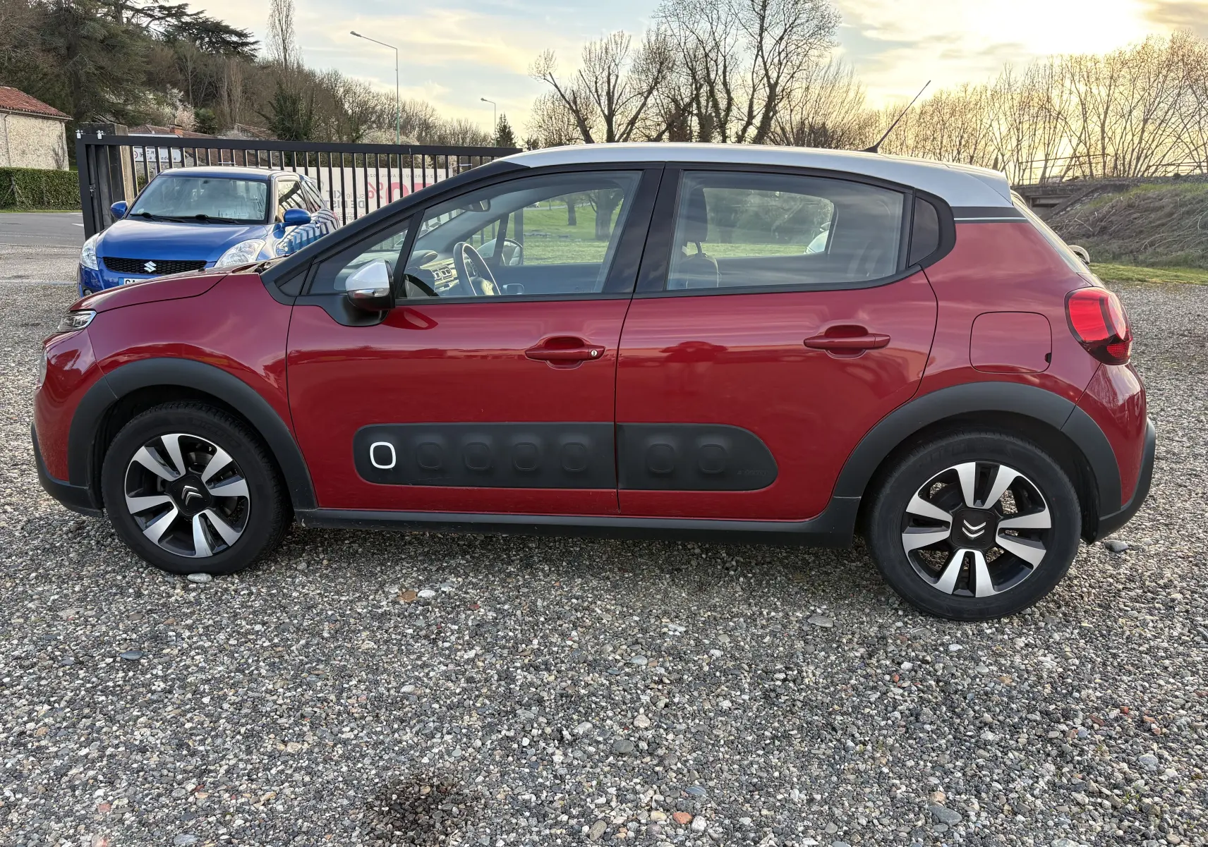 Vue de profil côté gauche d'une Citroën C3 rouge avec toit gris et protections Airbump noires sur les portières.