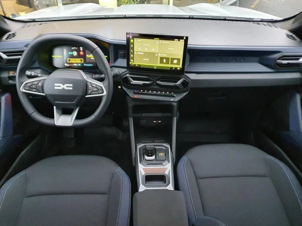 Vue intérieure avant du tableau de bord noir du Dacia Duster 1.6 Hybrid 140 avec écran tactile central et volant multifonction.