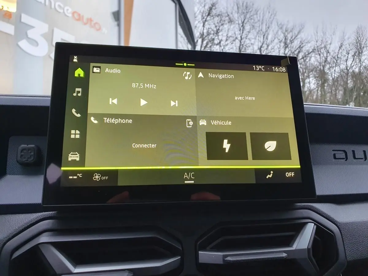 Écran tactile central du tableau de bord du Dacia Duster blanc glacier, affichant les menus audio et navigation.
