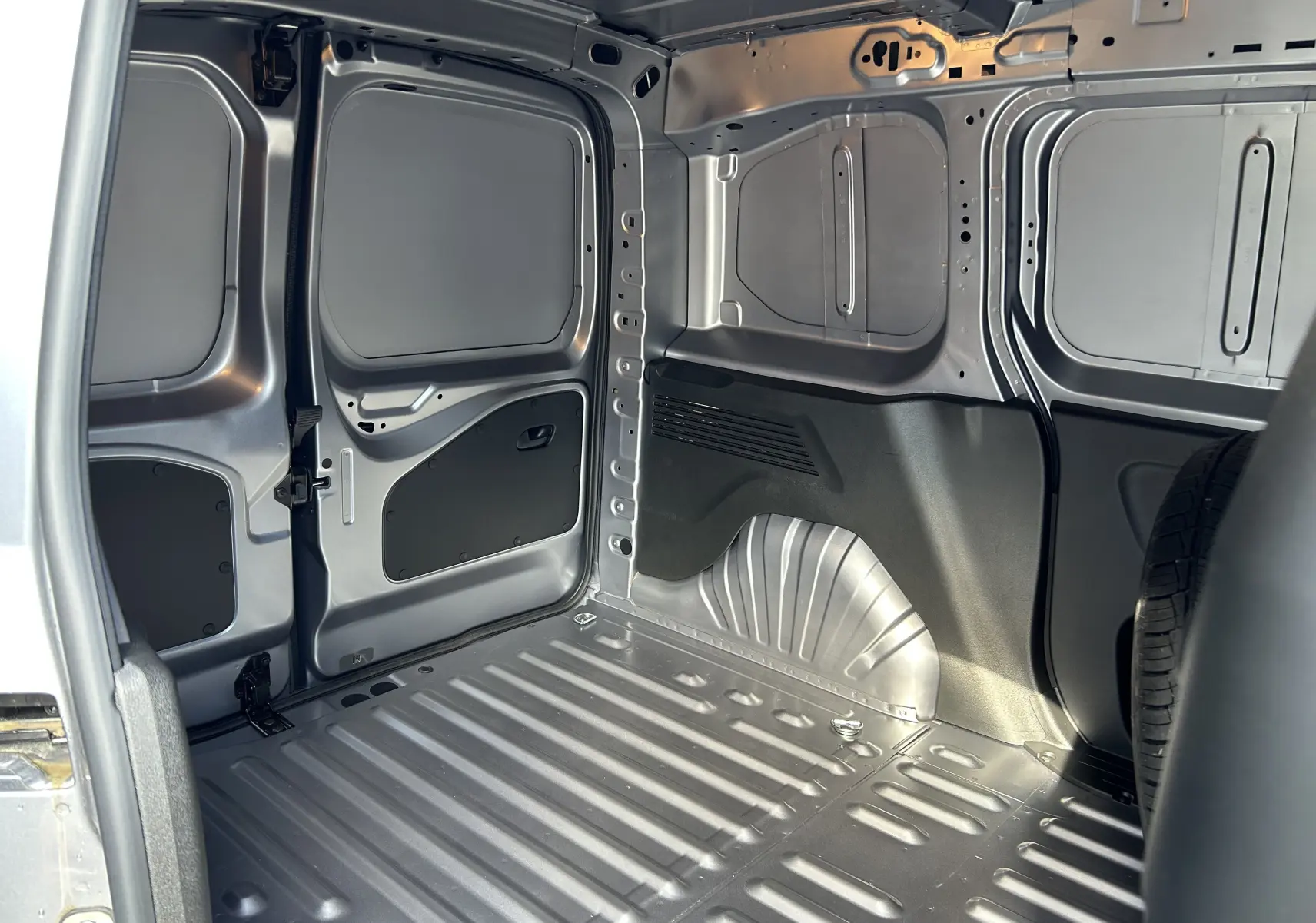 Intérieur du coffre du DANGEL Peugeot Partner 4x4 gris Artense, vue latérale droite montrant la structure métallique et une roue de secours.