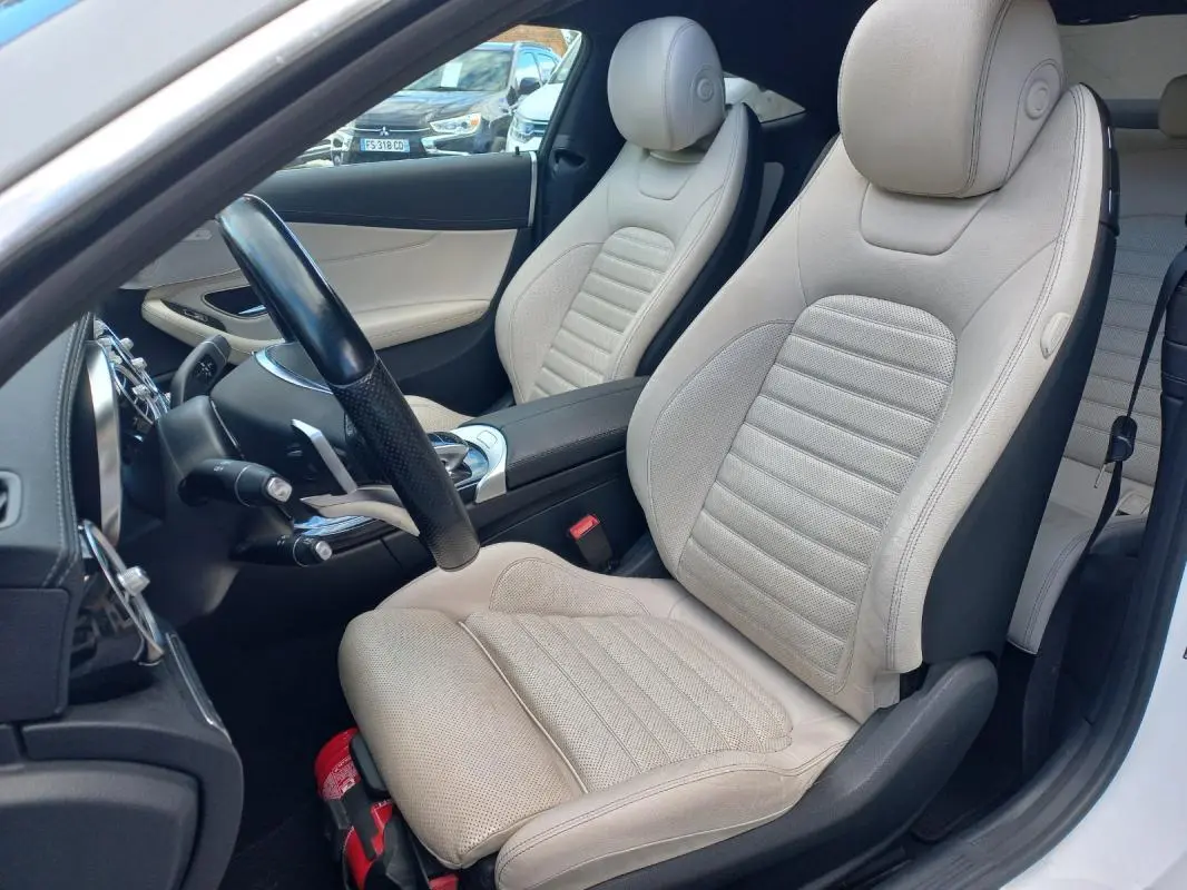 Vue intérieure côté conducteur d'une Mercedes Classe C Coupé 2016 avec sièges en cuir beige et volant multifonctions noir.