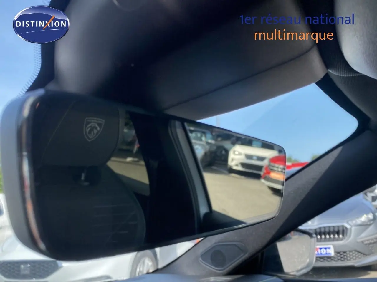 Rétroviseur intérieur de Peugeot 308 Hybrid blanc, avec reflet du logo lion sur appuie-tête et voitures en arrière-plan.