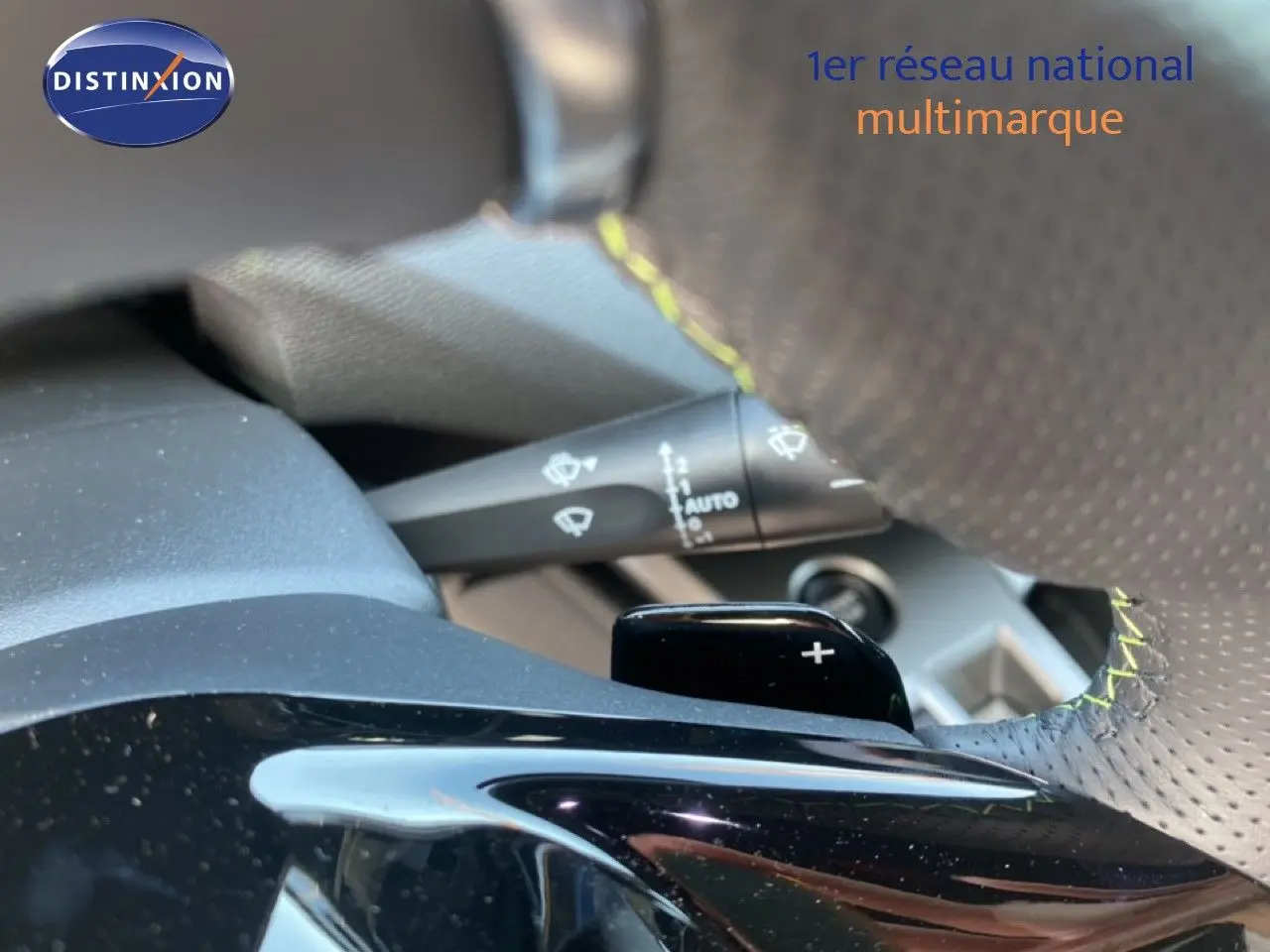 Gros plan sur le volant perforé avec surpiqûres jaunes et palettes de changement de vitesse d'une Peugeot 308 Hybrid blanche.