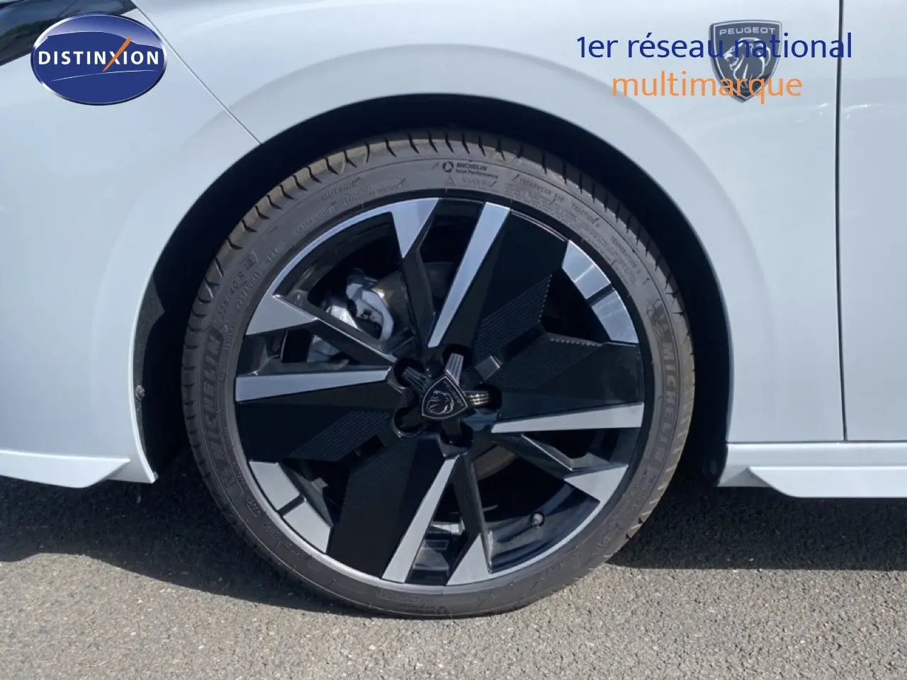 Gros plan sur la roue avant droite d'une Peugeot 308 Hybrid blanche, mettant en valeur la jante noire et argentée au design moderne.