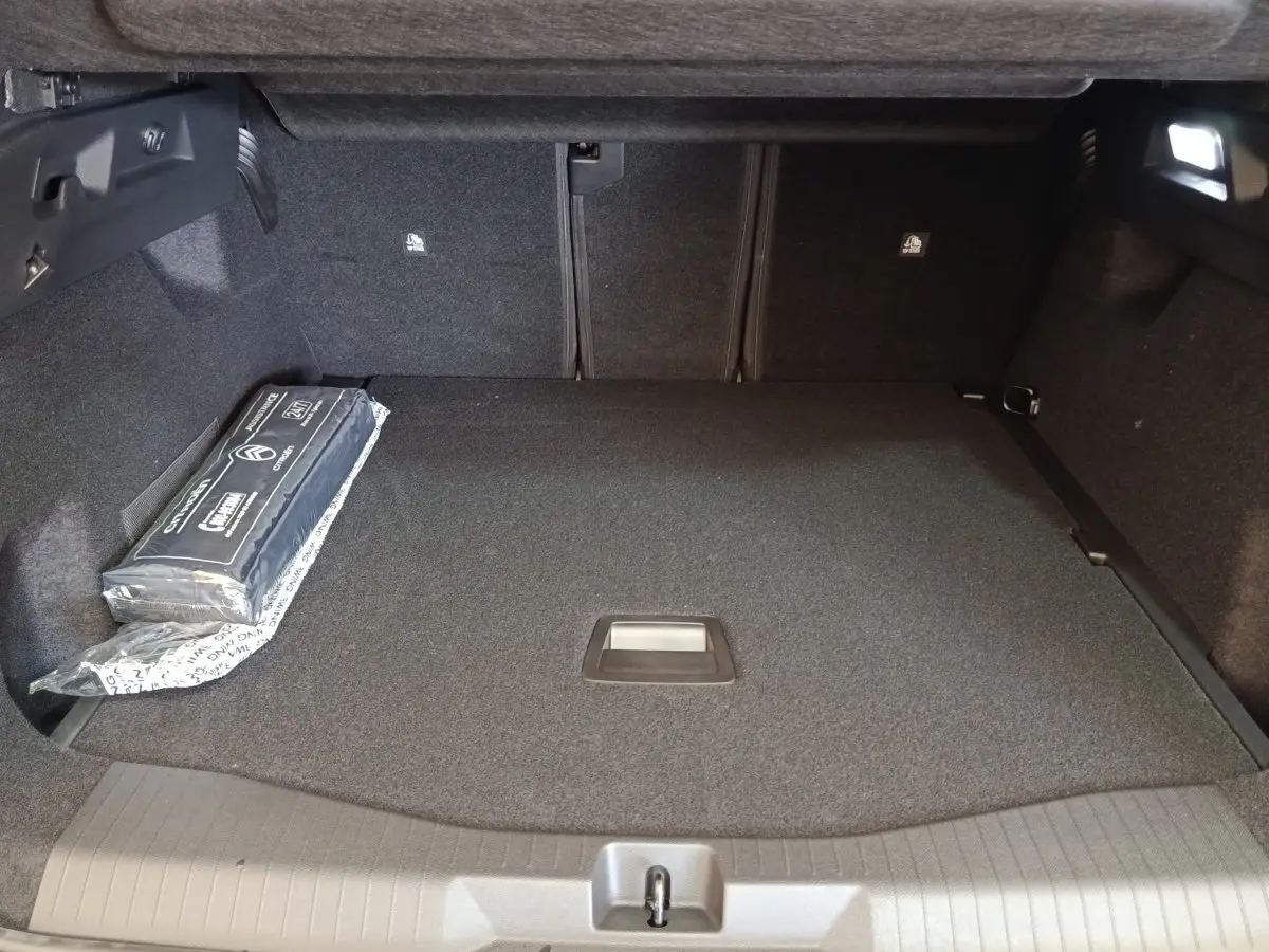 Coffre spacieux vu de face de la Citroën C5 Hybride 2026, avec tapis noir et kit de sécurité sur le côté gauche.