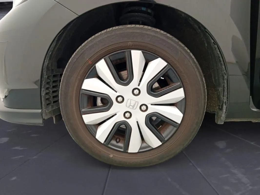 Gros plan sur la roue avant gauche noire d'une Honda Jazz 2024 E:HEV avec jante à design moderne bicolore.