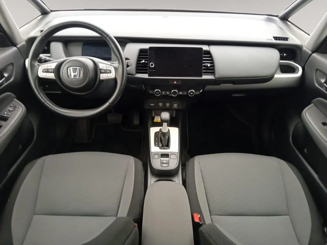 Vue intérieure avant de la Honda Jazz 2024 E:HEV Advance, tableau de bord noir avec écran tactile central et volant multifonction.