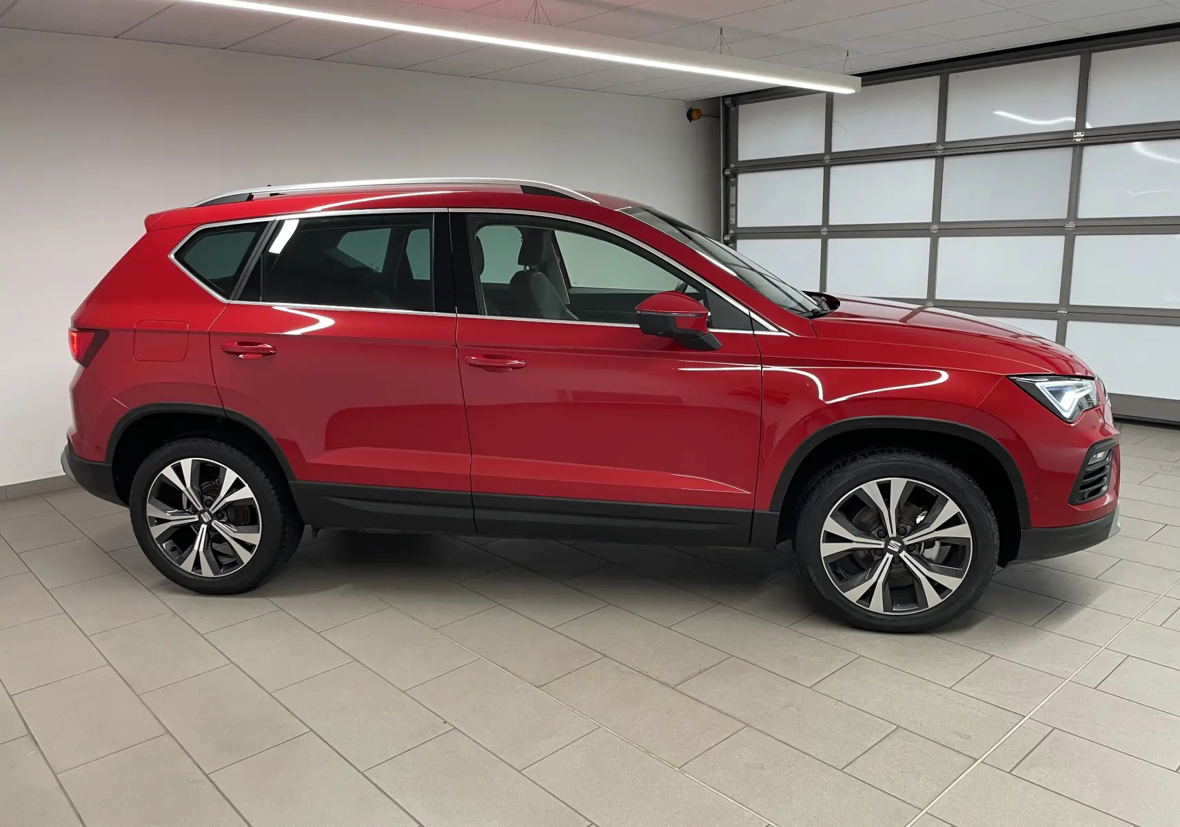Vue de profil côté gauche d'un SEAT Ateca 2024 Rouge Velvet avec jantes 18 pouces usinées dans un garage.