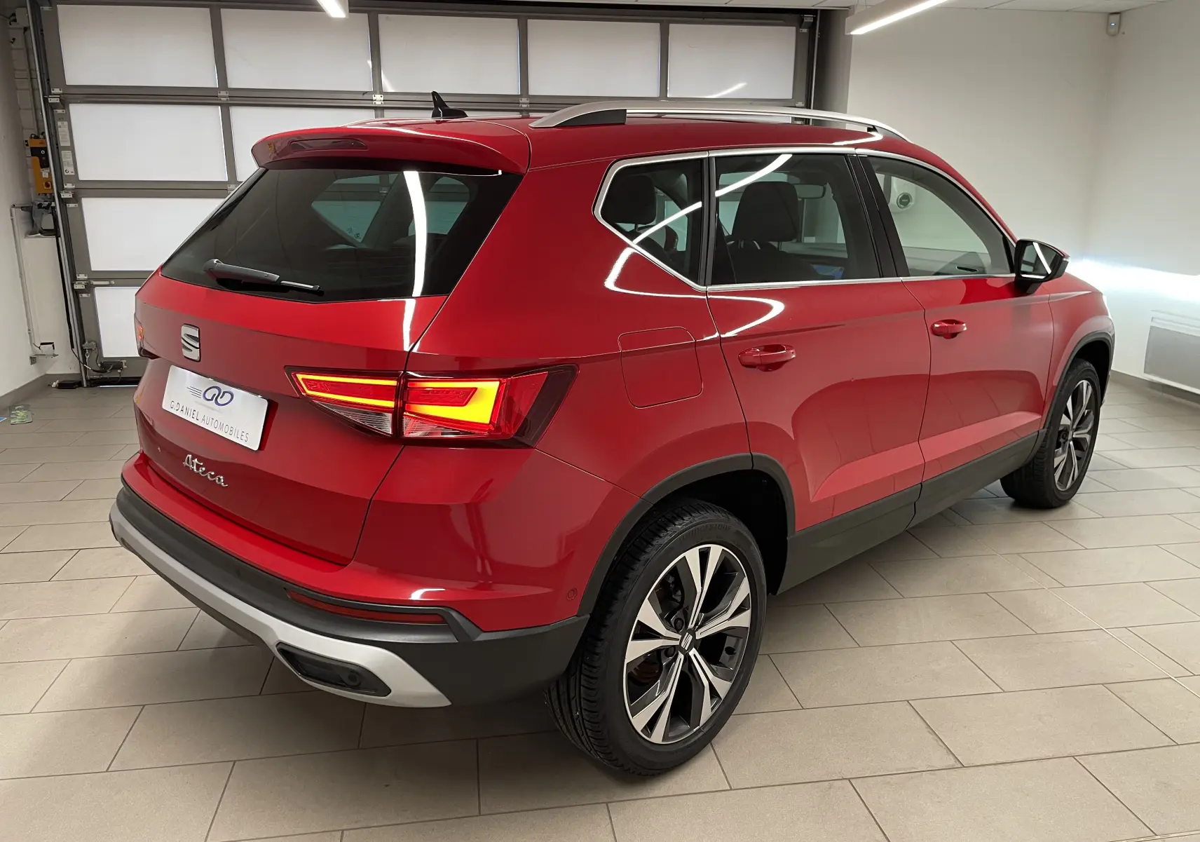 Vue 3/4 arrière droite du SEAT Ateca Rouge Velvet avec jantes 18 pouces usinées dans un garage éclairé.