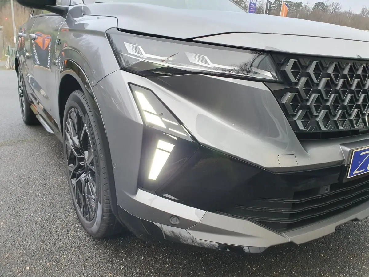 Gros plan sur l'avant droit du Renault Austral gris schiste avec calandre noire et feux LED allumés.