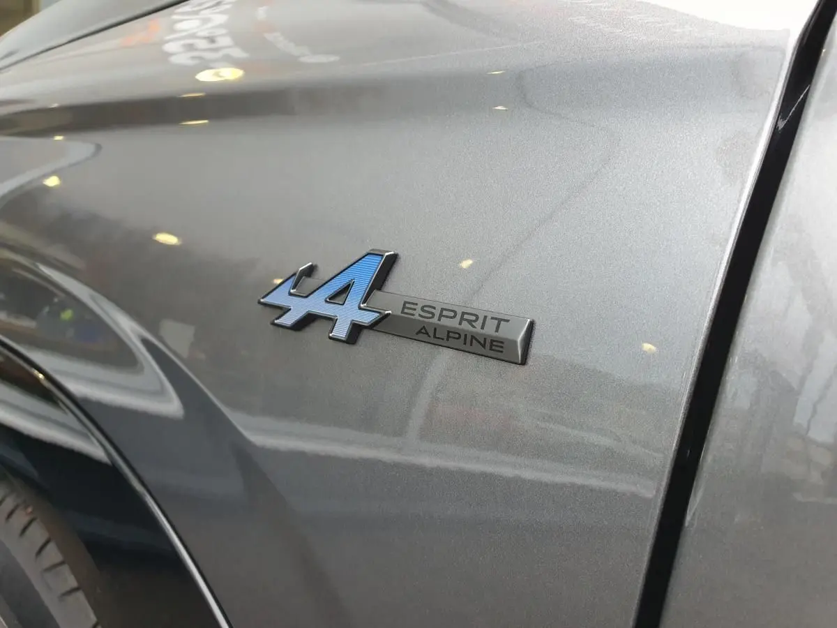 Gros plan sur l'emblème Esprit Alpine bleu sur l'aile avant droite d'un Renault Austral gris schiste.