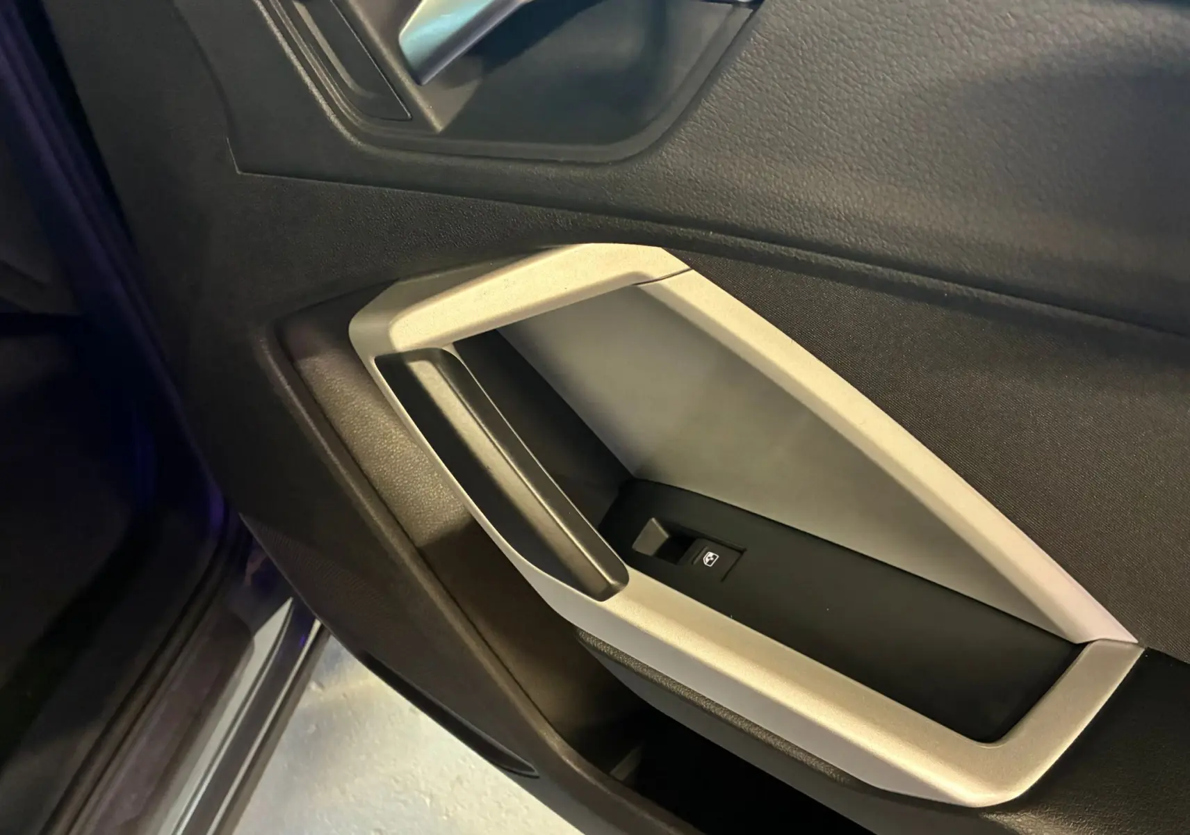 Détail de la poignée intérieure côté gauche de la porte d’un Audi Q3 Sportback gris, avec encadrement argent micrométallique.