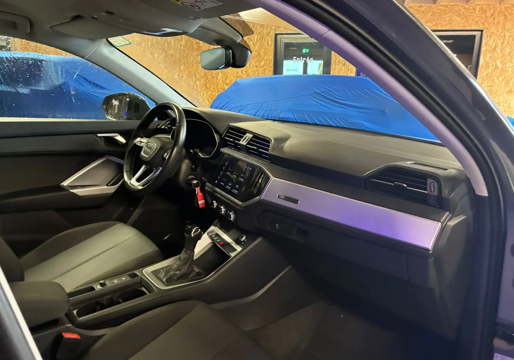 Vue intérieure côté conducteur de l'Audi Q3 Sportback gris, avec tableau de bord moderne et volant multifonctions cuir.