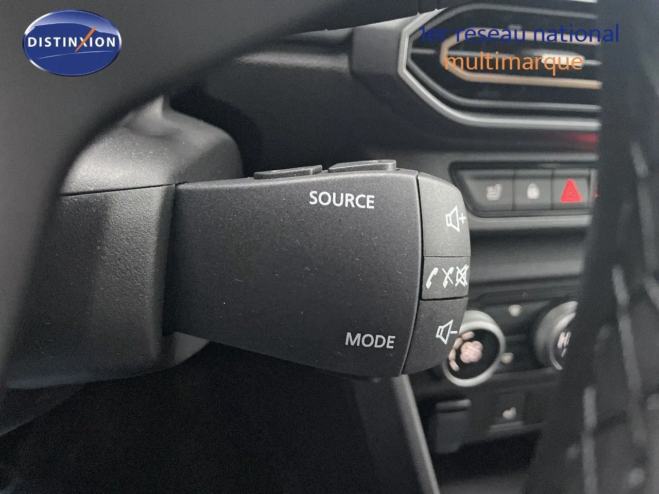 Gros plan sur la commande au volant du Dacia Jogger 2026, avec boutons source et mode, intérieur noir visible en arrière-plan.