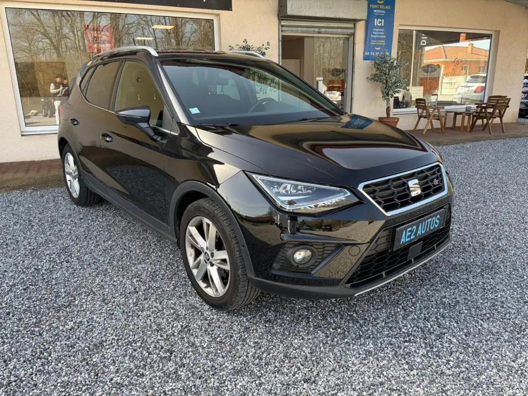 SEAT Arona noir vue 3/4 avant droit, avec calandre hexagonale et jantes alliage, stationné sur gravier devant un bâtiment.