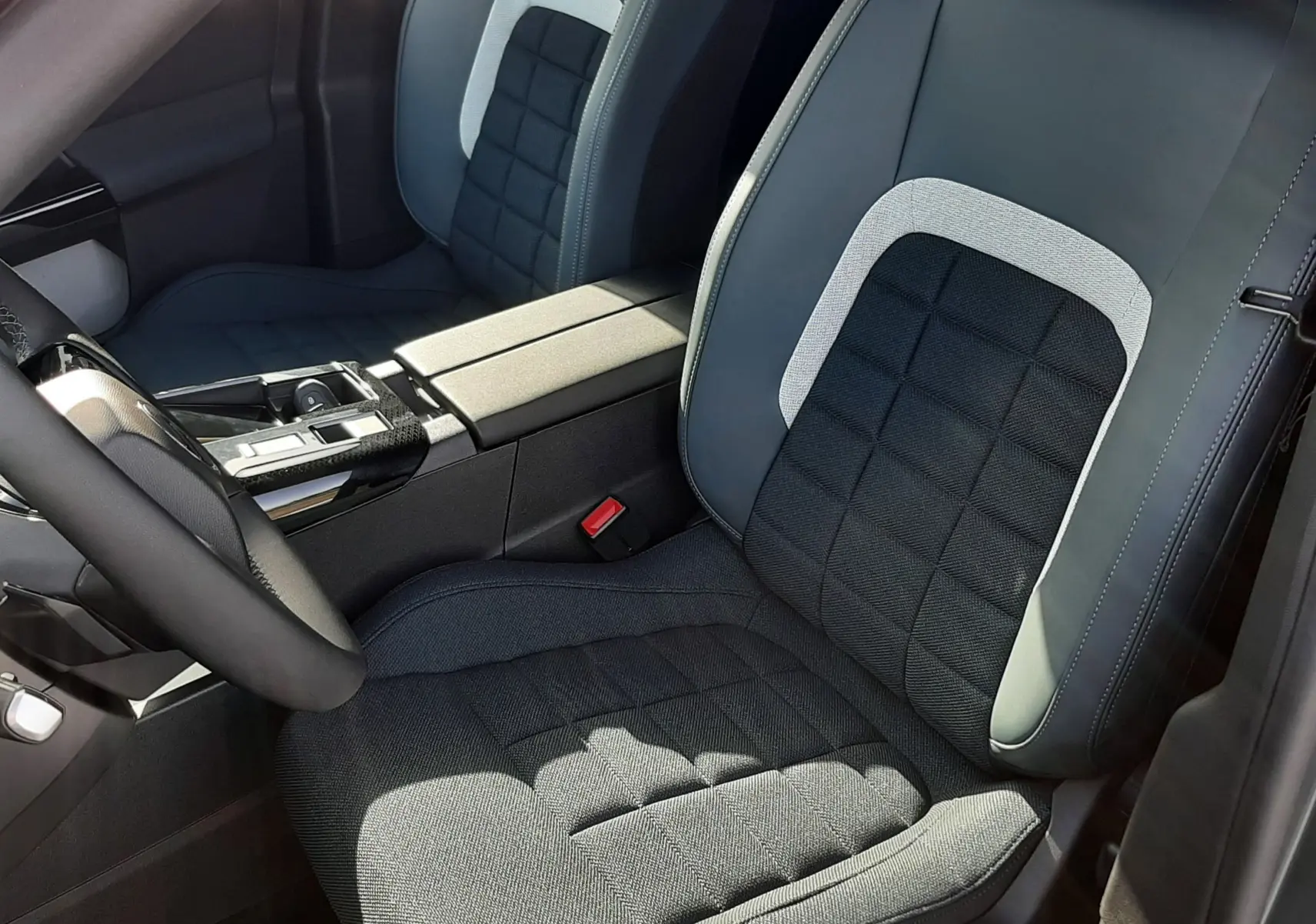 Vue intérieure rapprochée des sièges avant gris noir et tissu avec surpiqûres, console centrale et volant partiel visibles.