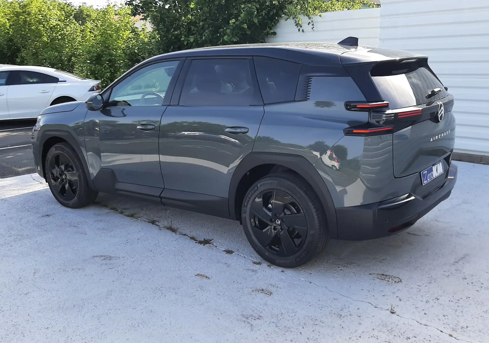 Vue 3/4 arrière droite d'un Citroën C5 Aircross vert Astoria avec toit noir et jantes noires, stationné en extérieur.