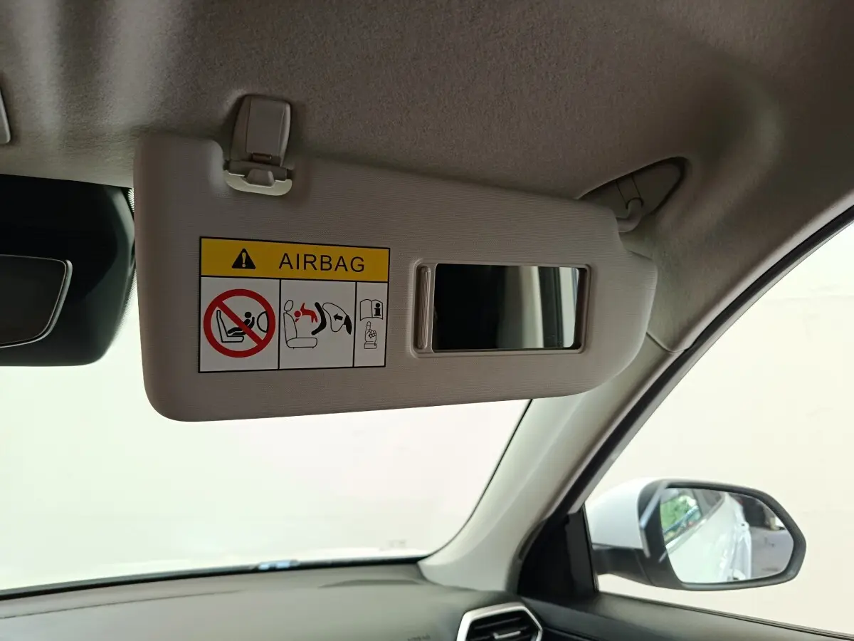Vue intérieure côté conducteur du pare-soleil beige avec miroir et avertissement airbag dans un MG ZS blanc hybride.