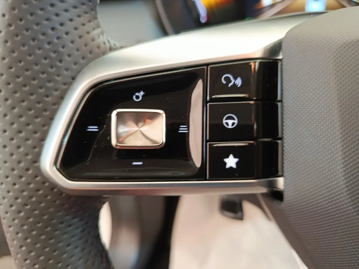 Gros plan sur les commandes noires et argentées du volant perforé côté gauche du MG ZS blanc hybride 2026.