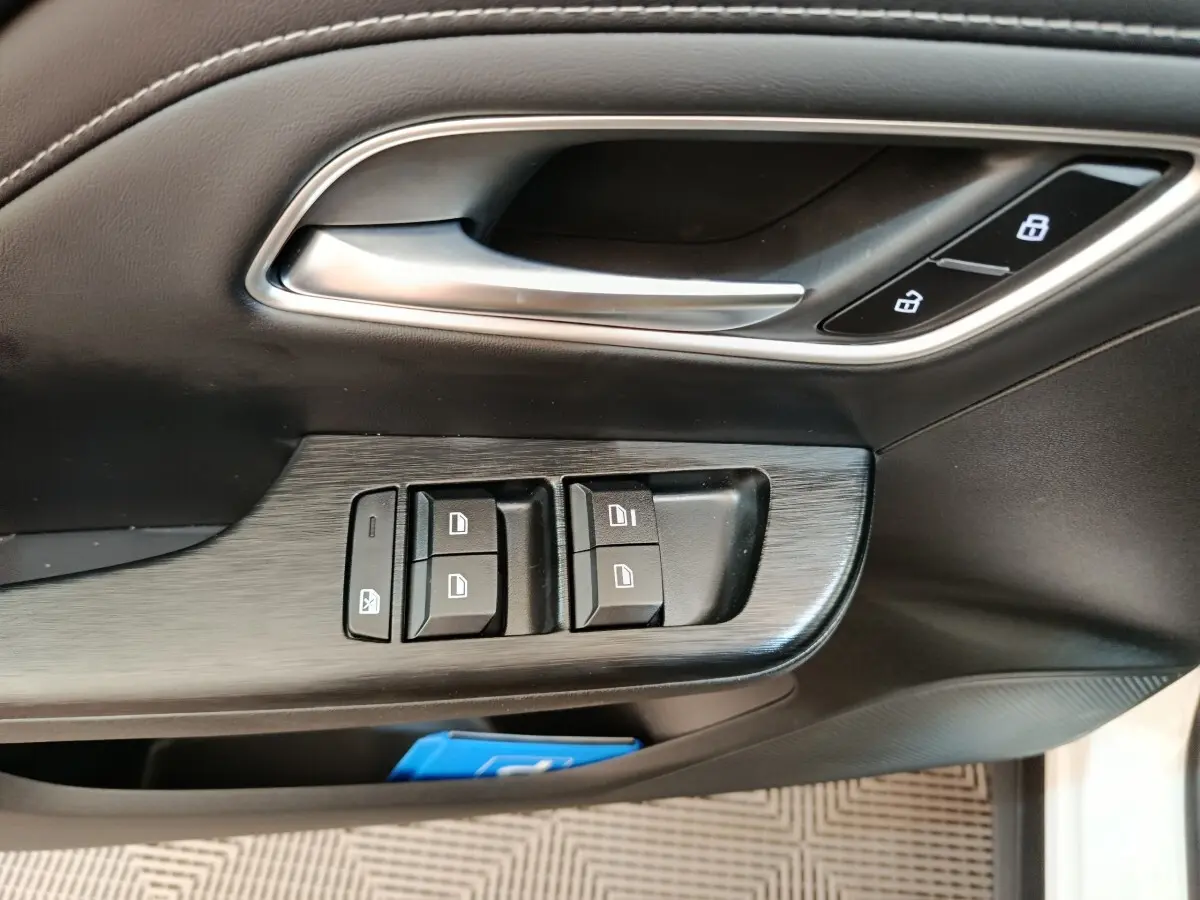 Gros plan sur la porte côté conducteur du MG ZS blanc, montrant les commandes de vitres et la poignée intérieure argentée.
