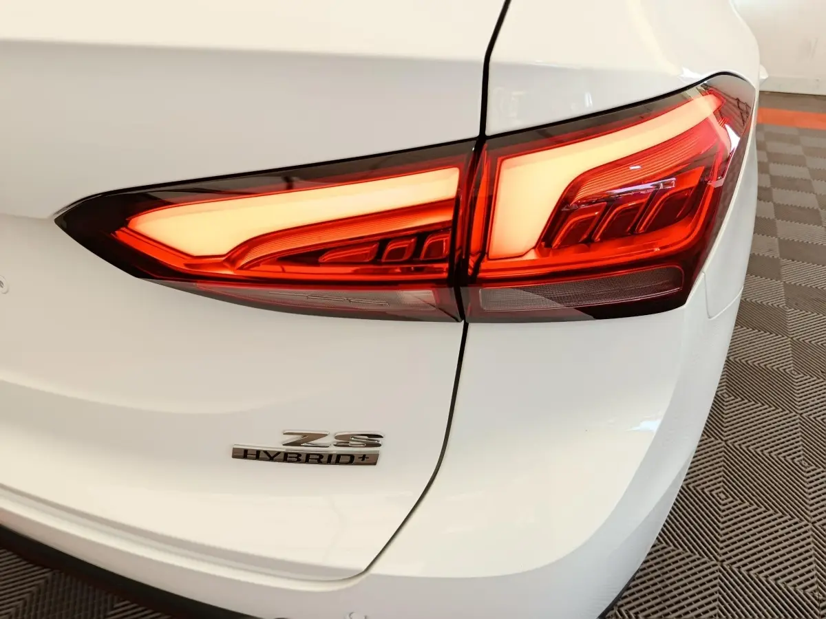 Gros plan sur le feu arrière droit et le logo Hybrid+ du MG ZS blanc, vue arrière côté droit.