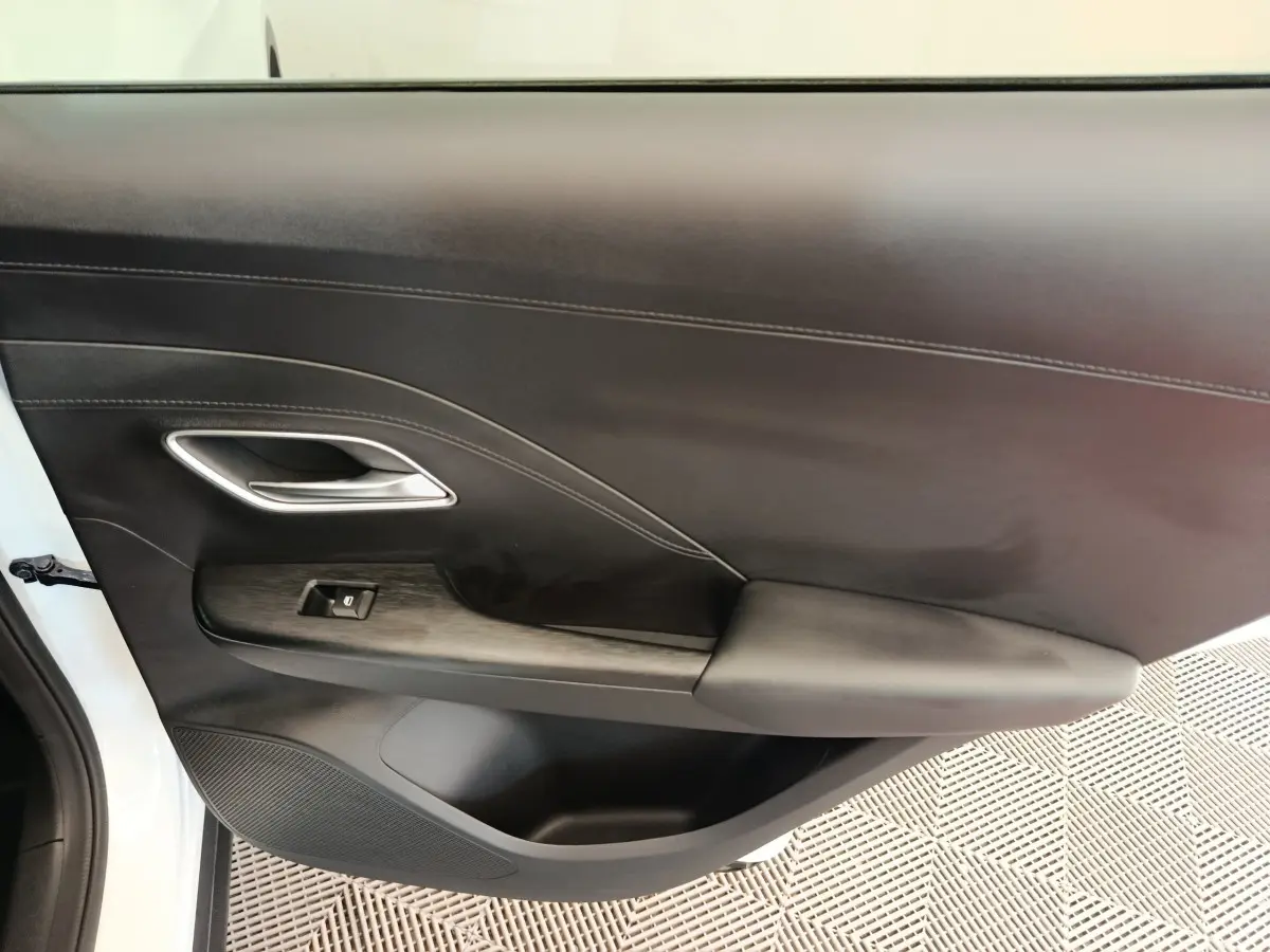 Vue intérieure côté gauche de la porte avant blanche du MG ZS 1.5L Hybrid+ Luxury avec accoudoir et commande de fenêtre.