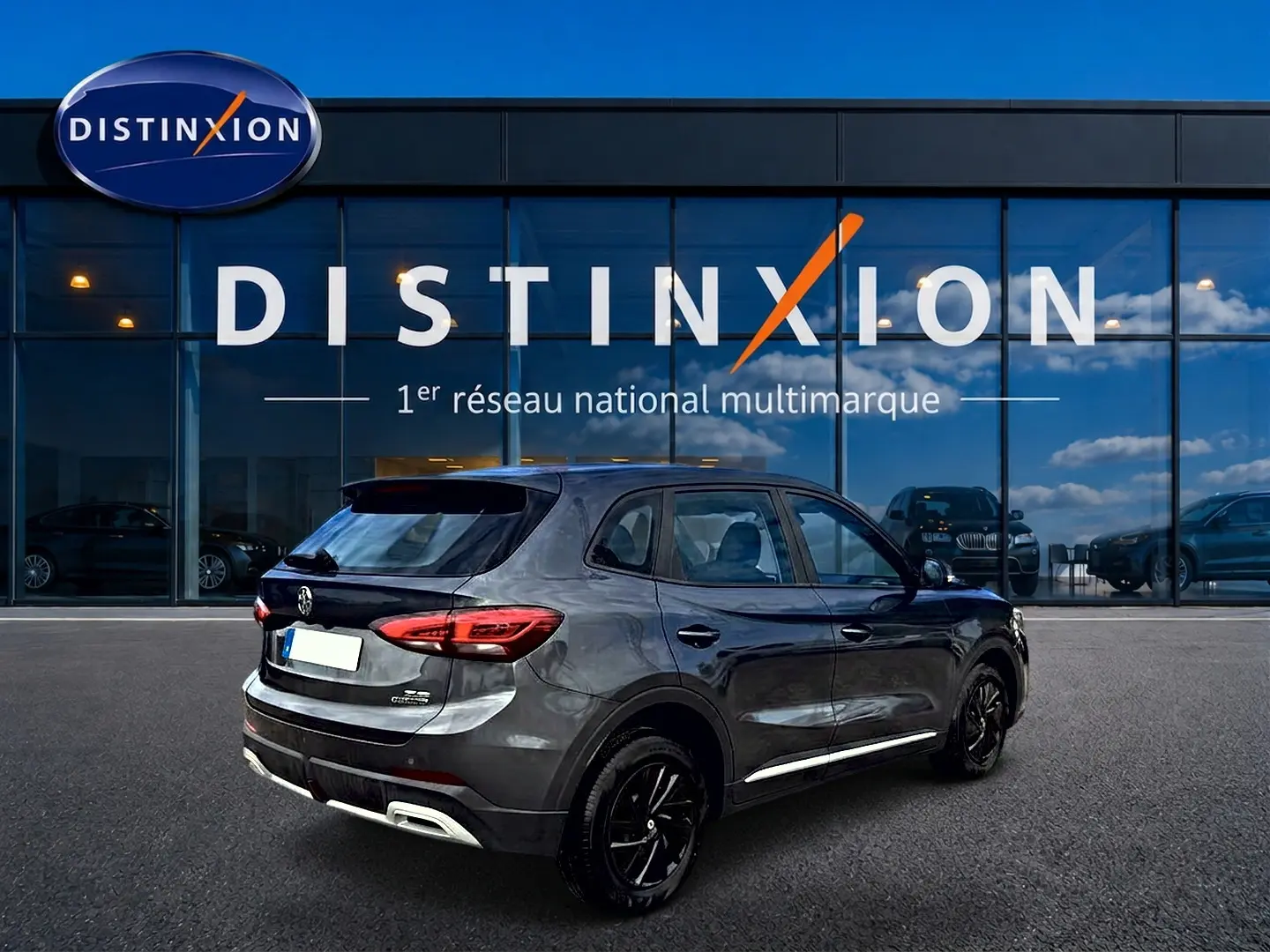 Vue 3/4 arrière droite du MG ZS 1.5 hybrid Camden grey, avec feux arrière LED et jantes noires devant un showroom Distinxion.