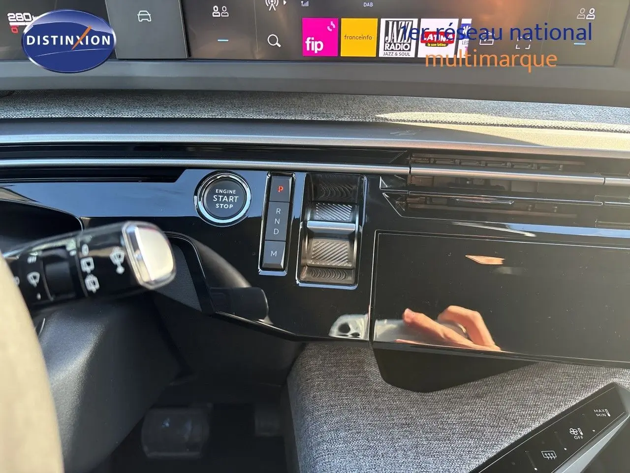 Vue rapprochée de la console centrale noire brillante du Peugeot 5008 hybride 2025, avec bouton start/stop et commandes de boîte auto.