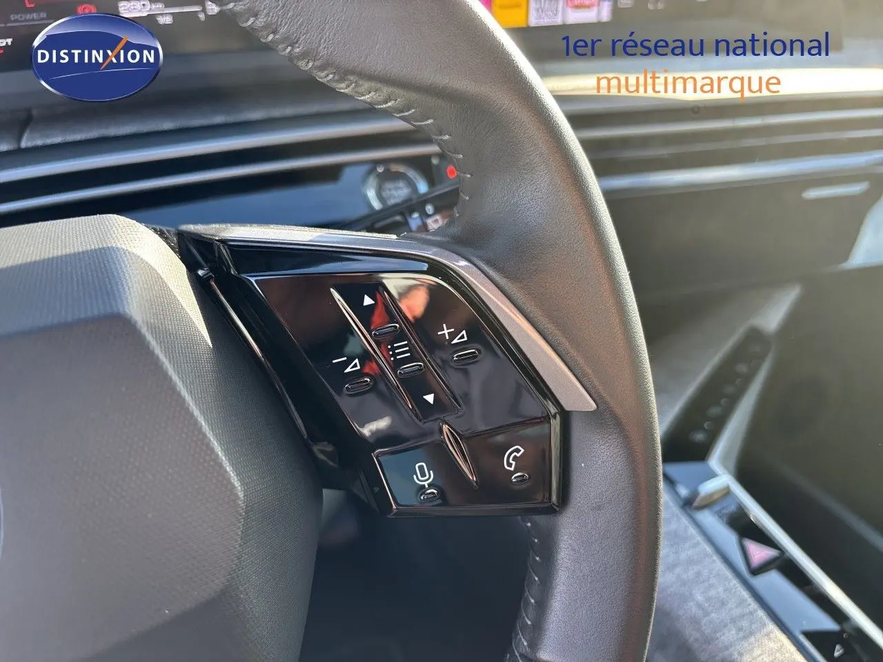 Gros plan sur les commandes multifonctions noires du volant côté gauche du Peugeot 5008 blanc Okenite, intérieur moderne.