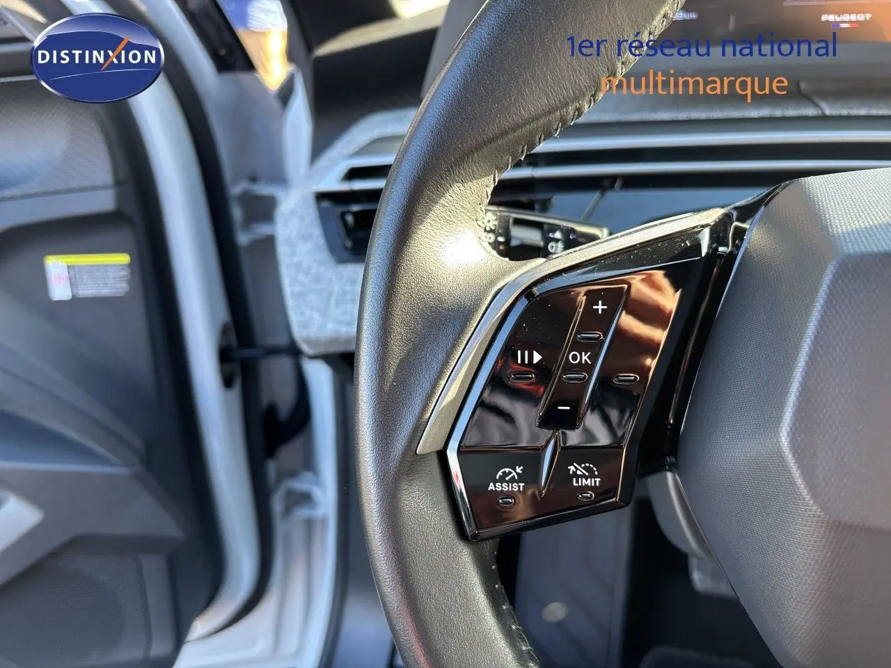 Vue rapprochée du volant noir du Peugeot 5008 blanc Okenite 2025, avec commandes multifonctions visibles côté gauche.