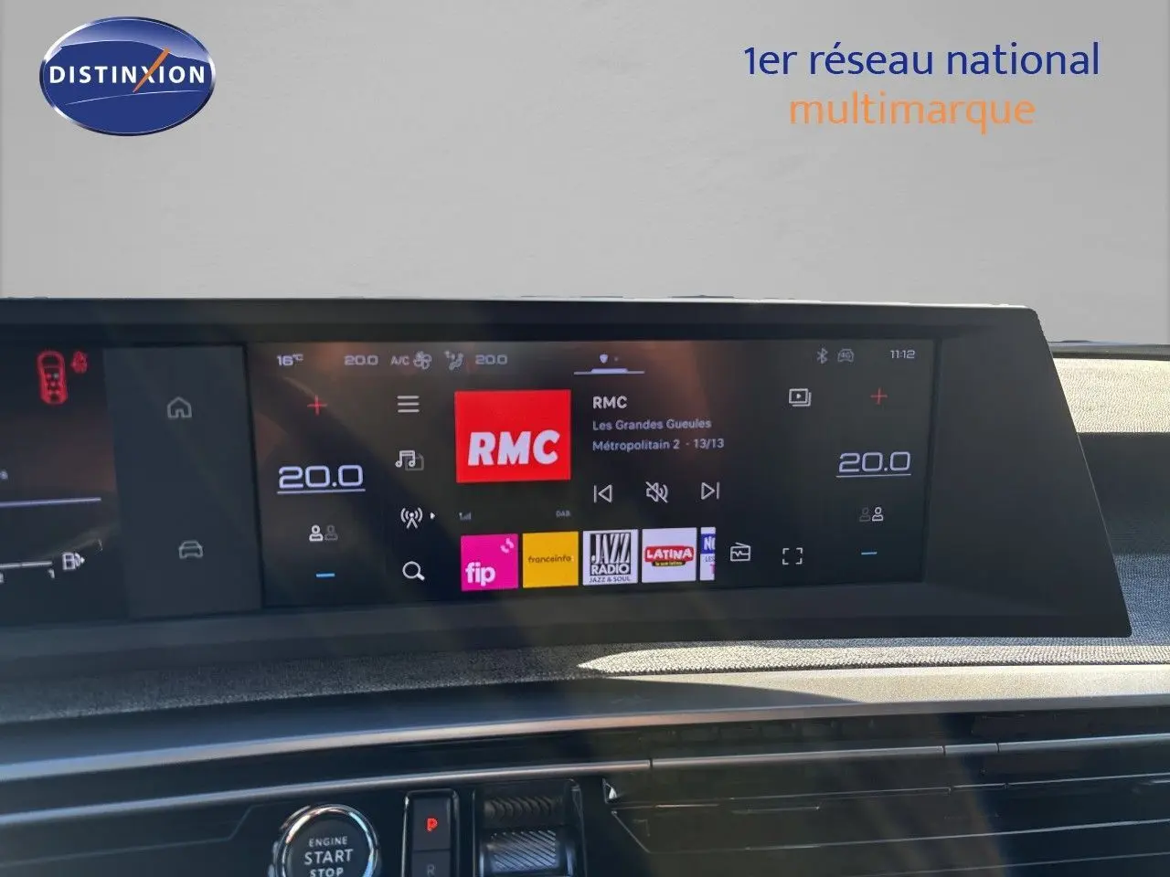 Écran tactile central du tableau de bord du Peugeot 5008 hybride 2025 affichant la radio RMC et la climatisation à 20°C.