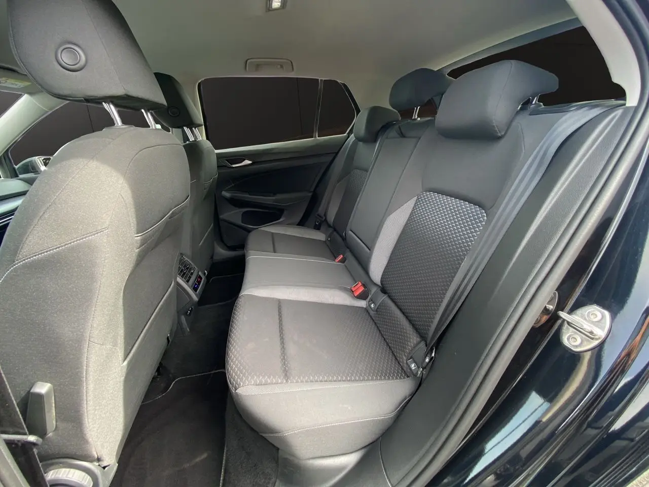 Vue intérieure côté droit sur la banquette arrière noire en tissu de la Volkswagen Golf VIII 2022 avec vitres surteintées.