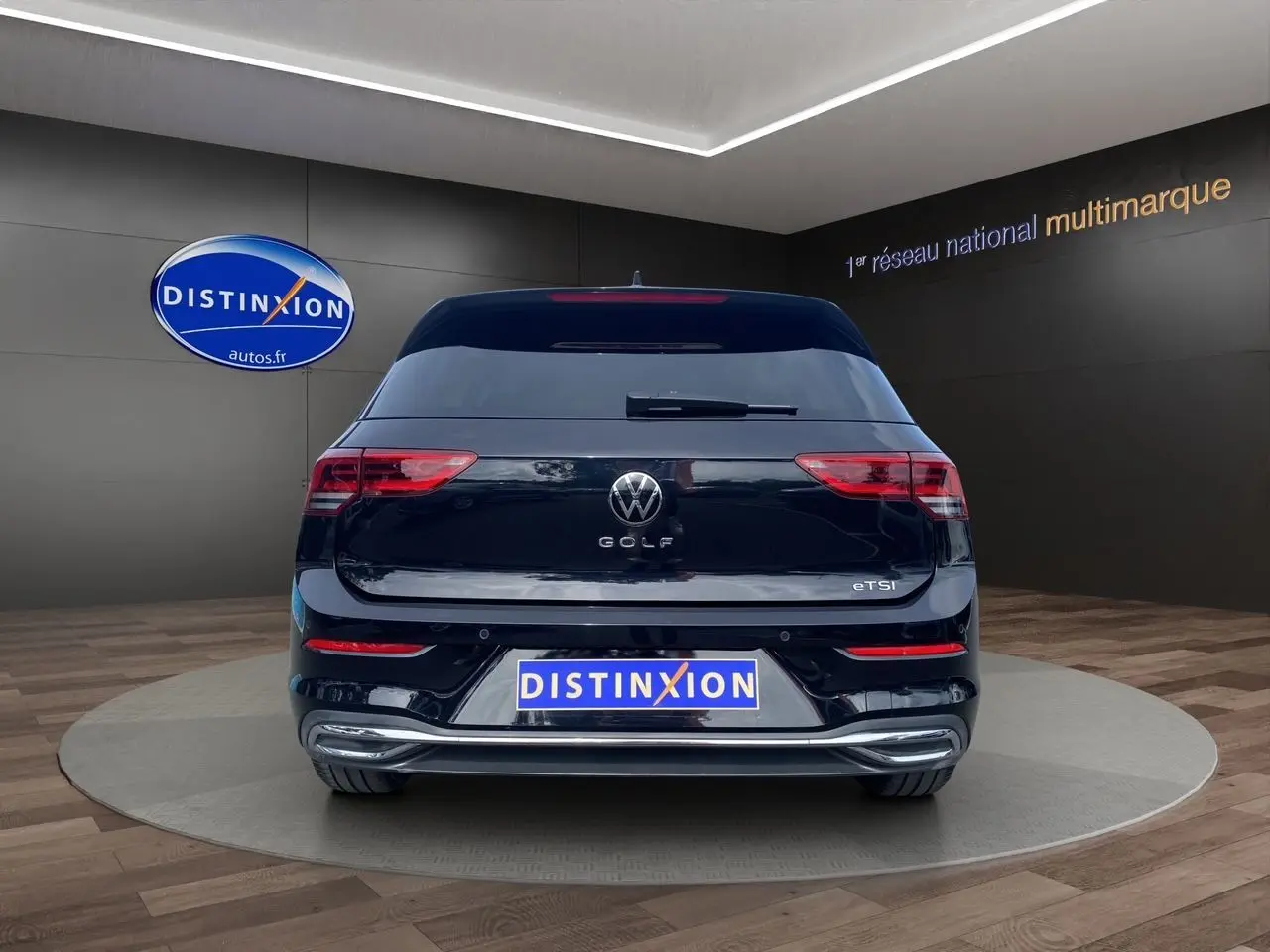 Vue arrière d'une Volkswagen Golf VIII noire avec logo et feux arrière allumés en showroom.