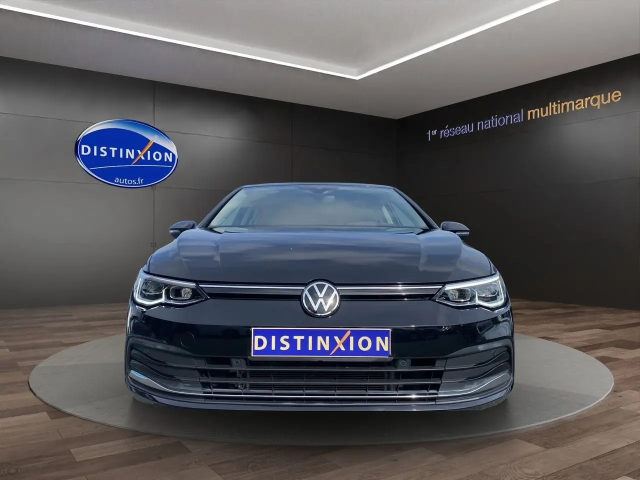 Vue frontale d'une Volkswagen Golf VIII noire, avec calandre et phares LED, dans un showroom Distinxion.