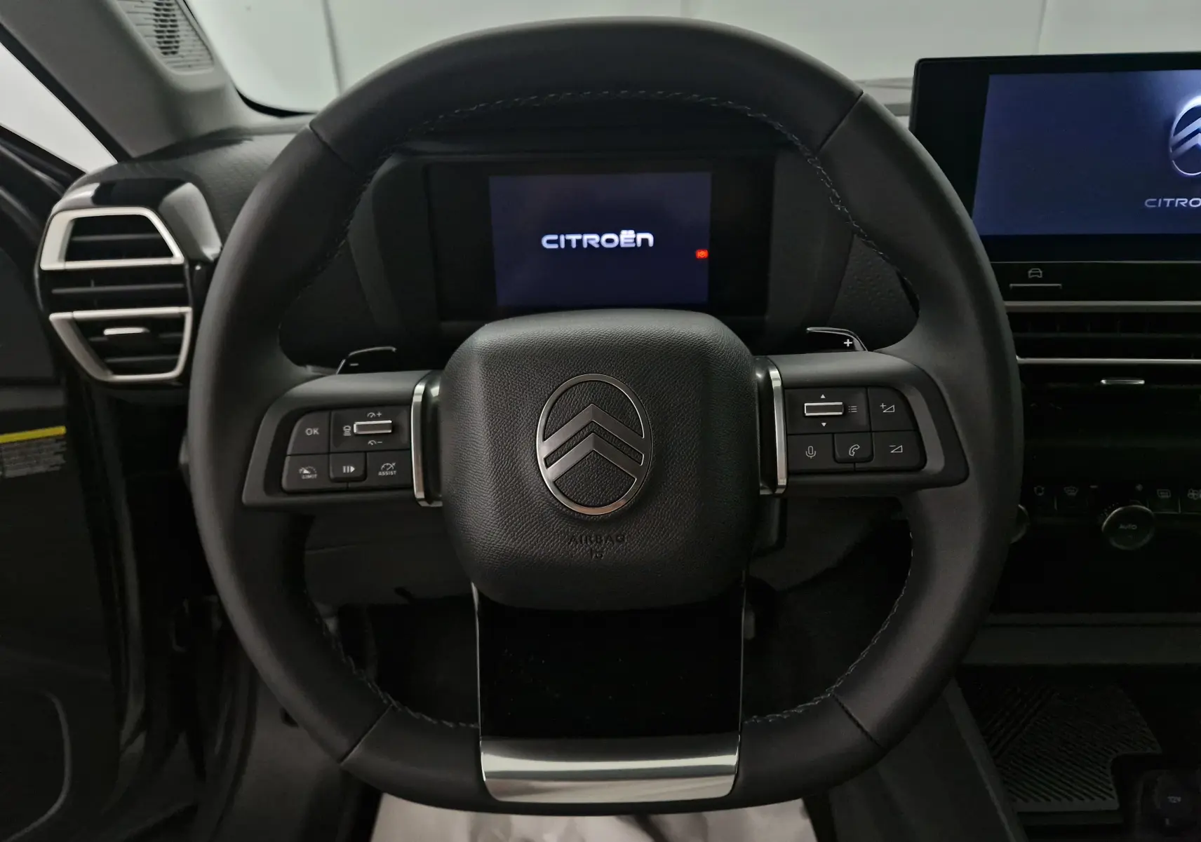 Vue rapprochée du volant cuir noir du Citroën C4 2025 avec commandes intégrées et écran digital en arrière-plan.