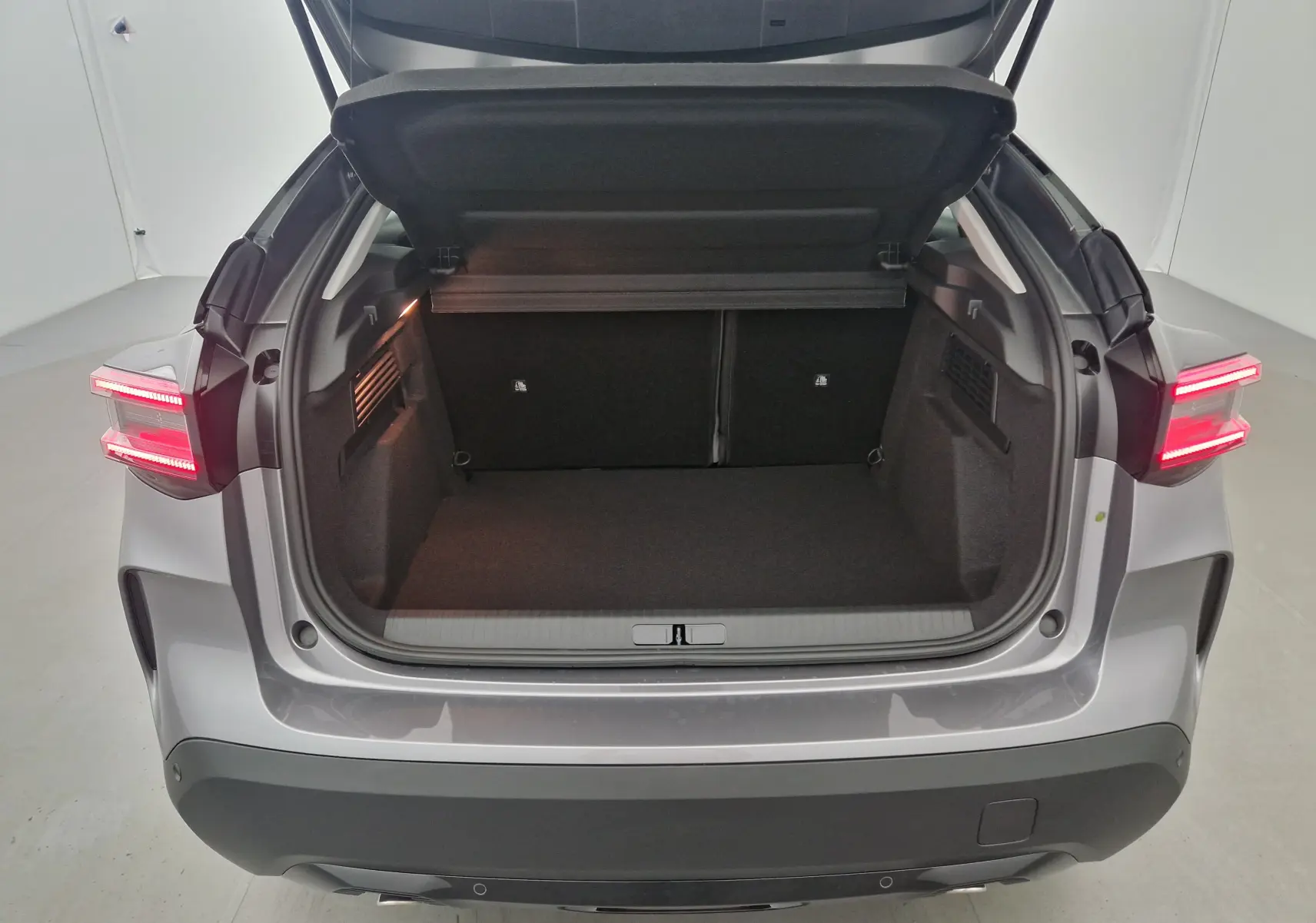 Coffre ouvert vu de l'arrière d'une Citroën C4 2025 gris Mercury et noir avec feux arrière allumés.