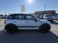 Vue de profil côté gauche d'une MINI Countryman Cooper 122 Pack Chili blanche, roues noires, sur un parking en plein jour.