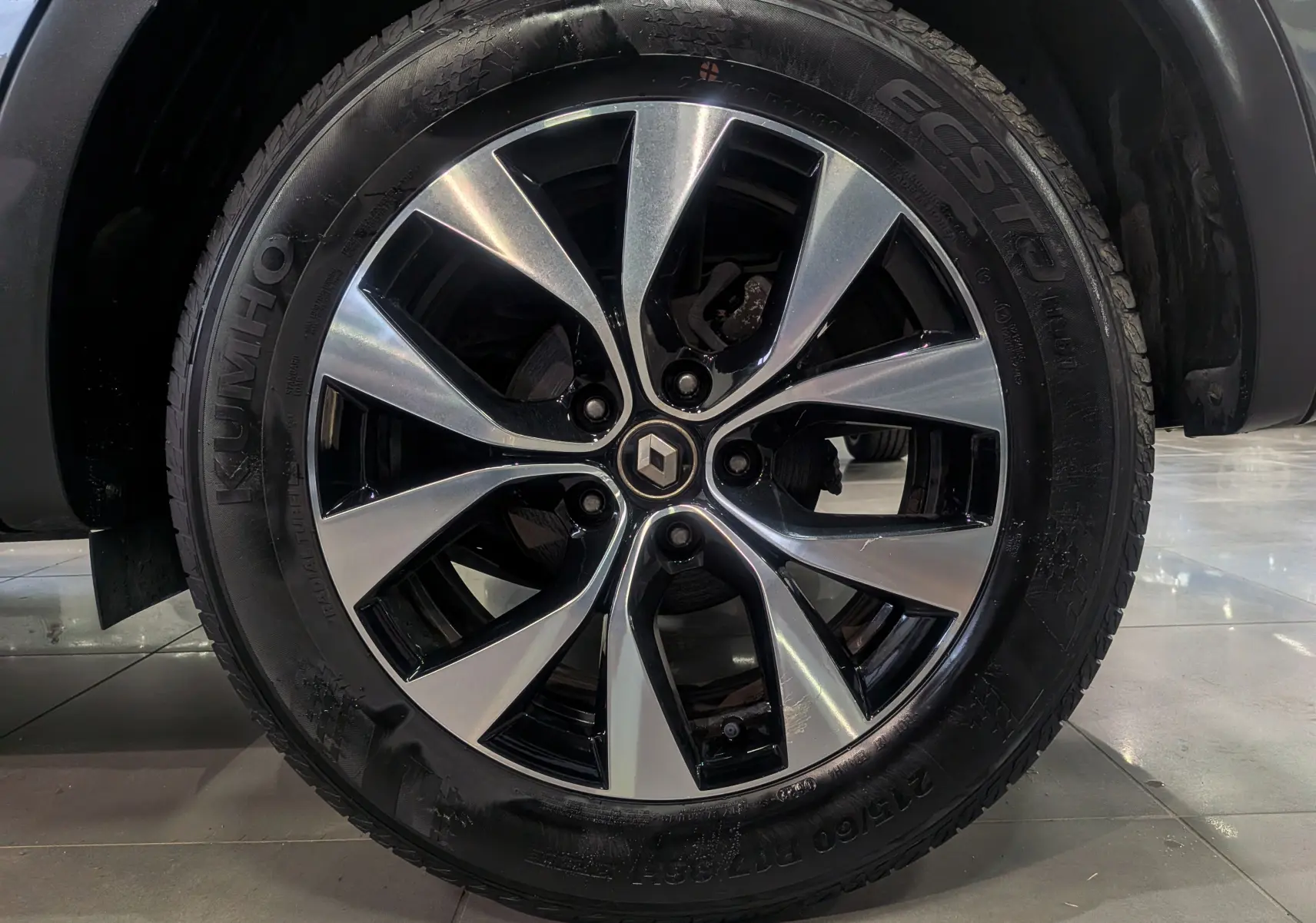 Gros plan sur la jante alliage biton avec logo Renault au centre, montée sur un pneu Kumho d’un Renault Arkana gris métal.
