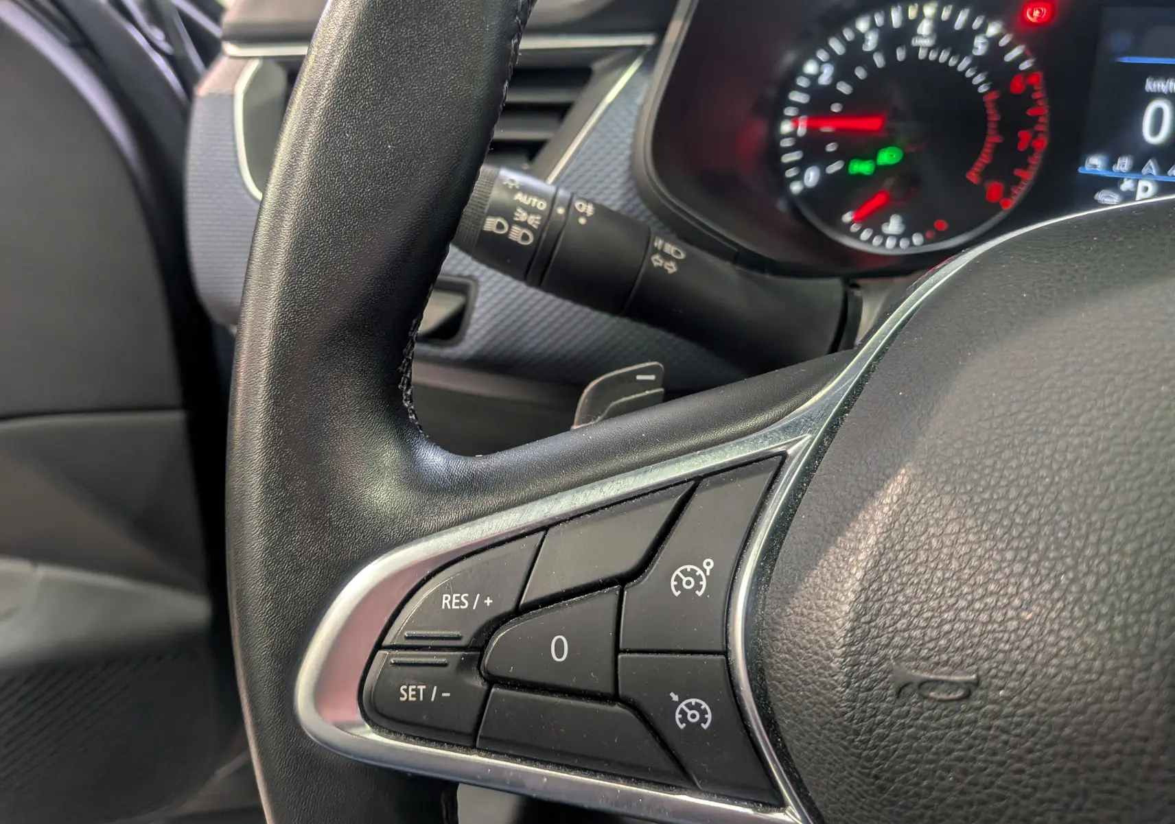 Gros plan sur le volant noir de la Renault Arkana 2022, avec commandes de régulateur de vitesse et tableau de bord partiellement visible.
