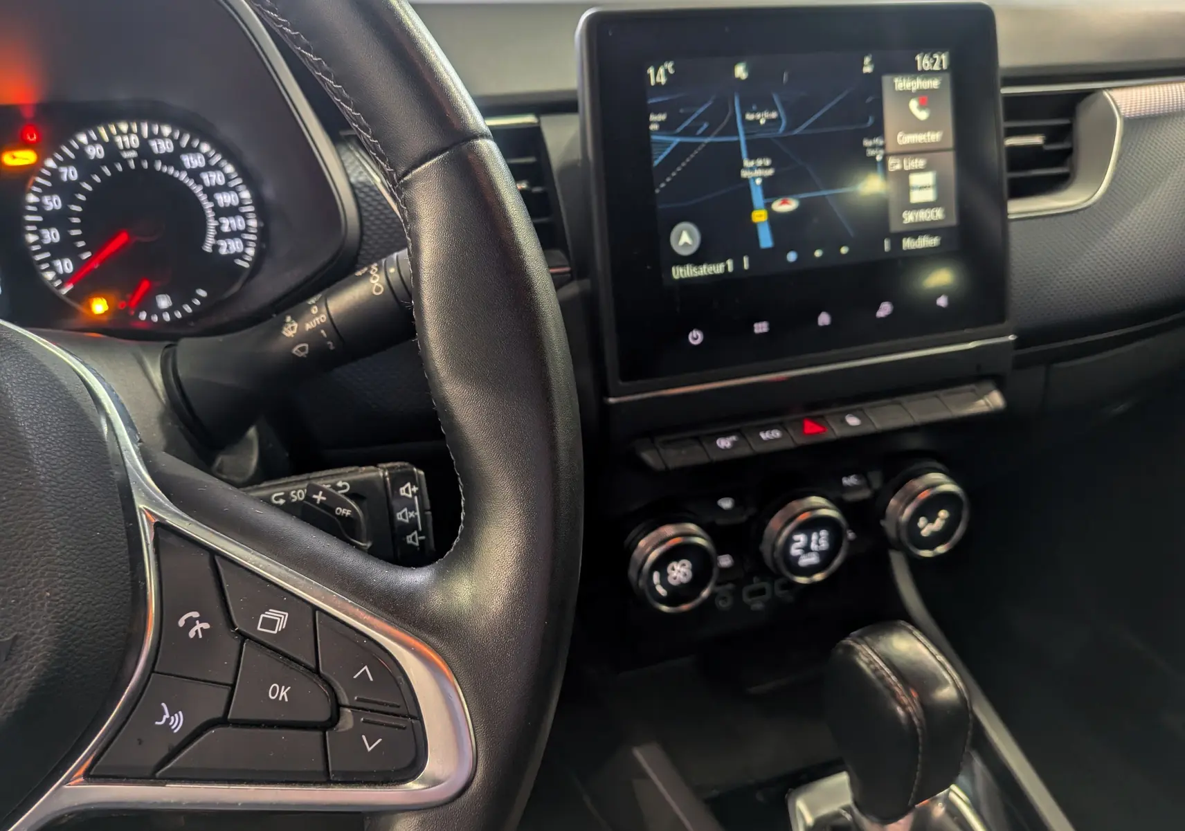 Vue intérieure centrée sur le volant et l’écran tactile du tableau de bord du Renault Arkana gris métal 2022 hybride.